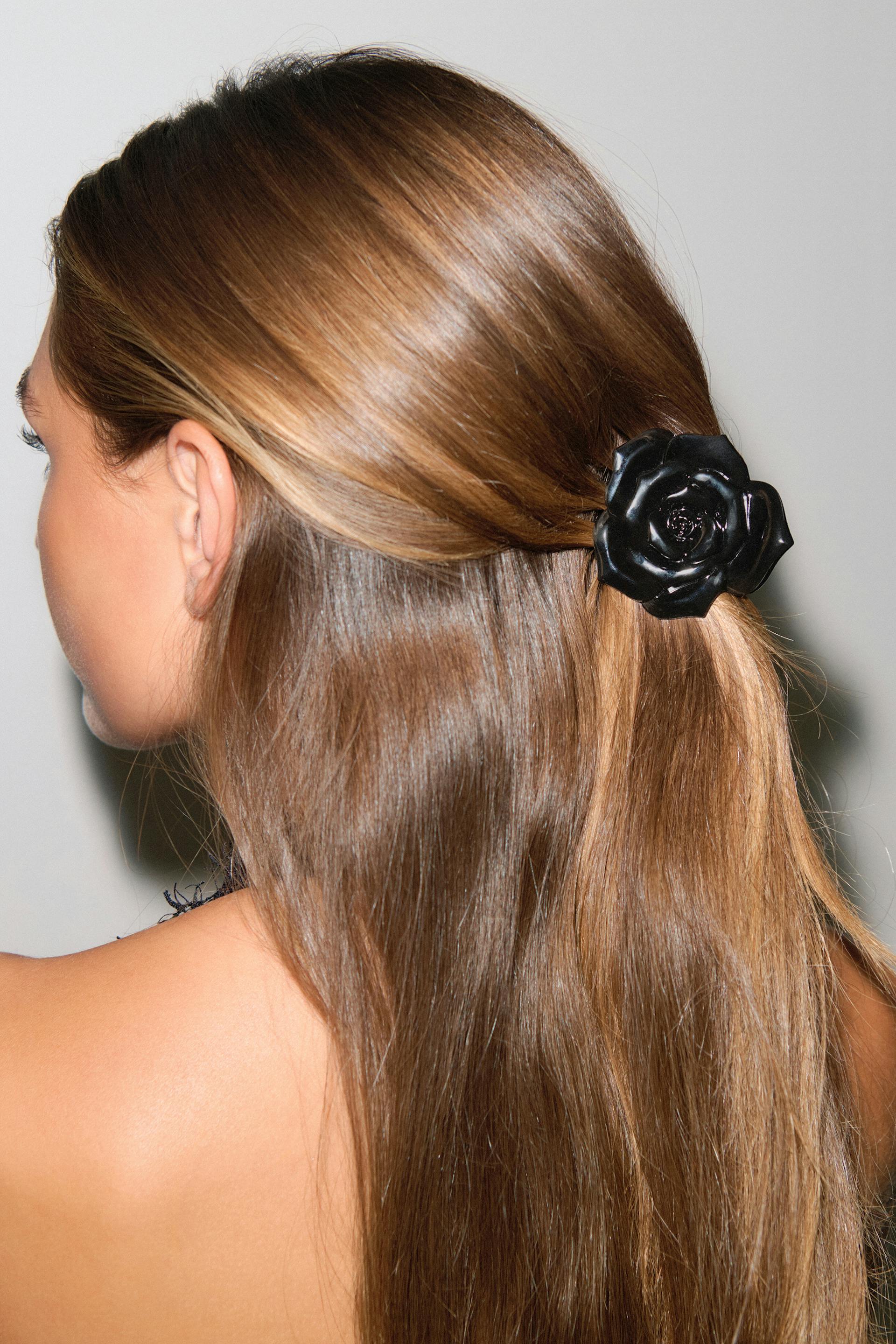 Black glossy rose-shaped hair clip securing a half-up hairstyle.