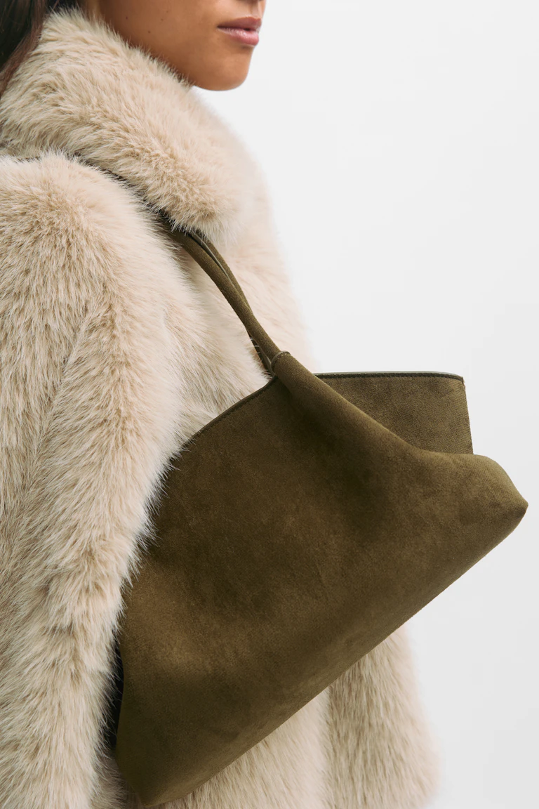 Manteau en fausse fourrure beige-crème associé à un sac à bandoulière en daim vert-olive avec une seule lanière sur le dessus.