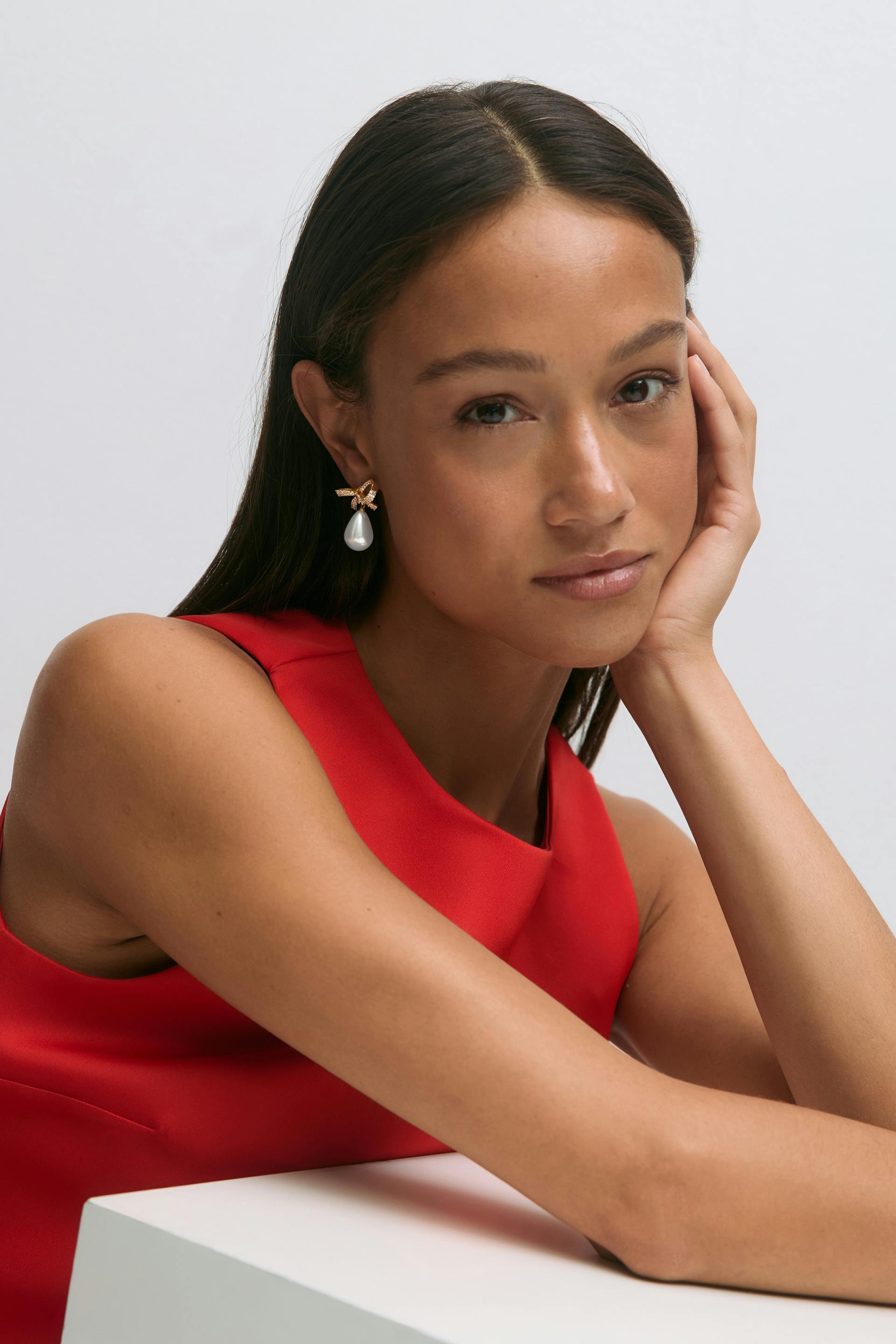 Hihaton punainen korkeakaulainen mekko yhdistettynä kultaisiin rusettikorvakoruihin, joissa on pisarapintaisia helmiriipuksia.