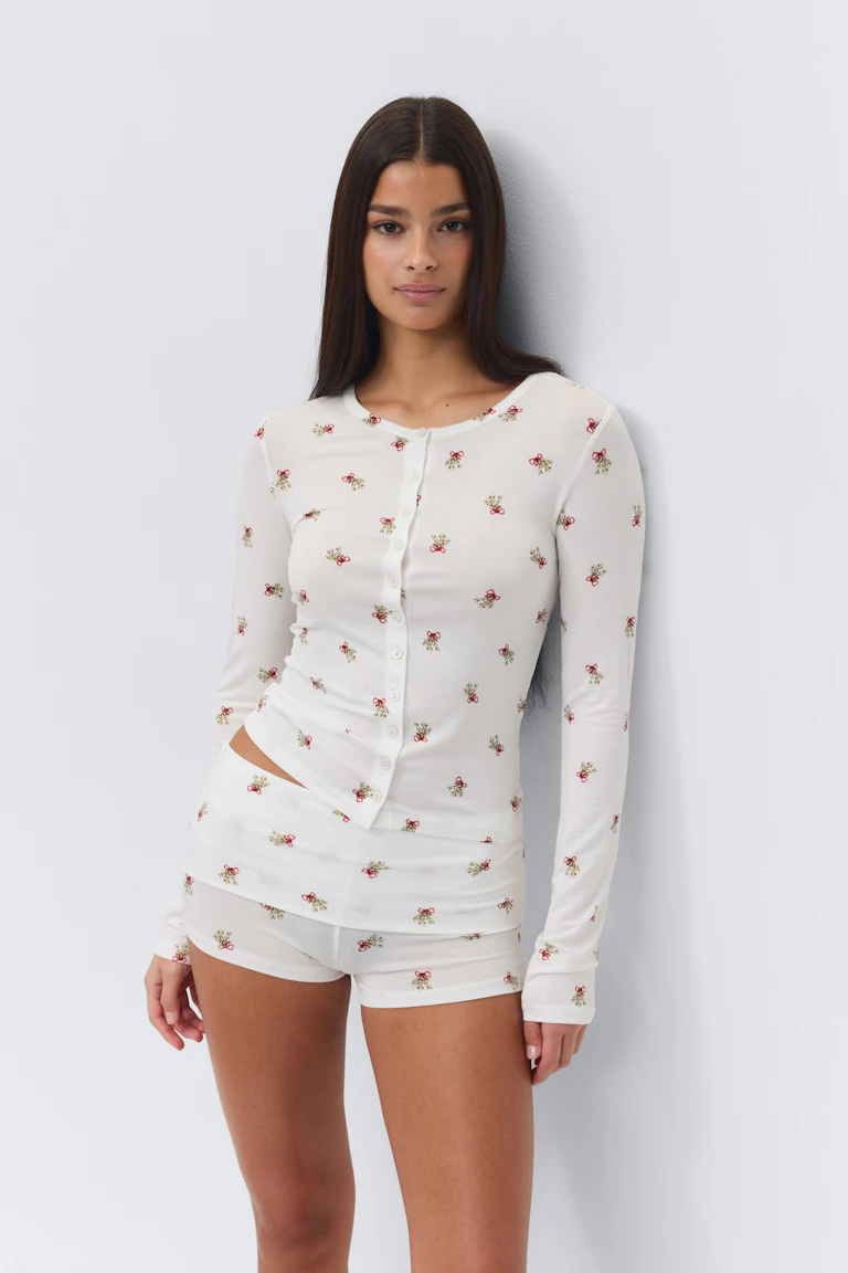 Witte geribde top met lange mouwen en knoopsluiting, gecombineerd met een bijpassende witte short, beide met een kleine all-overprint van rode bloemen en groene bladeren.