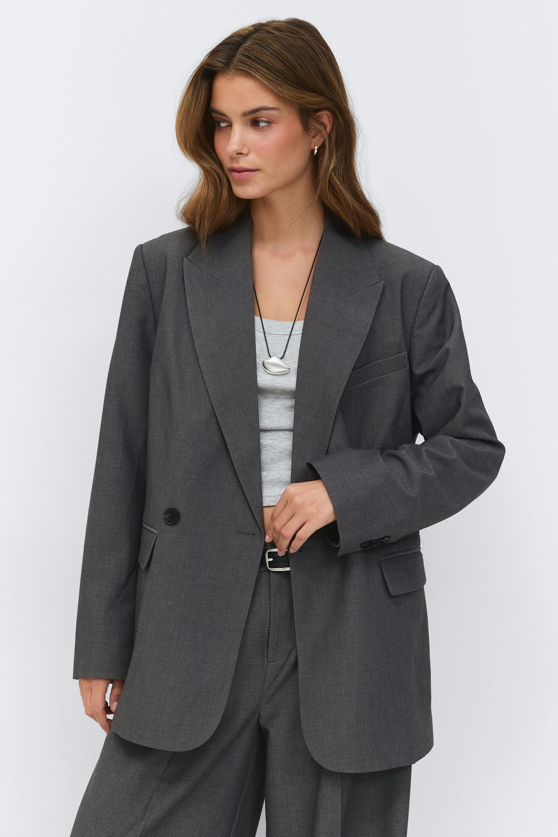 Hiilenvärinen yksirivinen ylisuuri bleiseri ja siihen sopivat leveälahkeiset housut, jotka on yhdistetty vaaleanharmaaseen kylkikangastoppiin, mustaan vyöhön, jossa on hopeinen solki, ja hopeiseen riipuskaulakoruun.