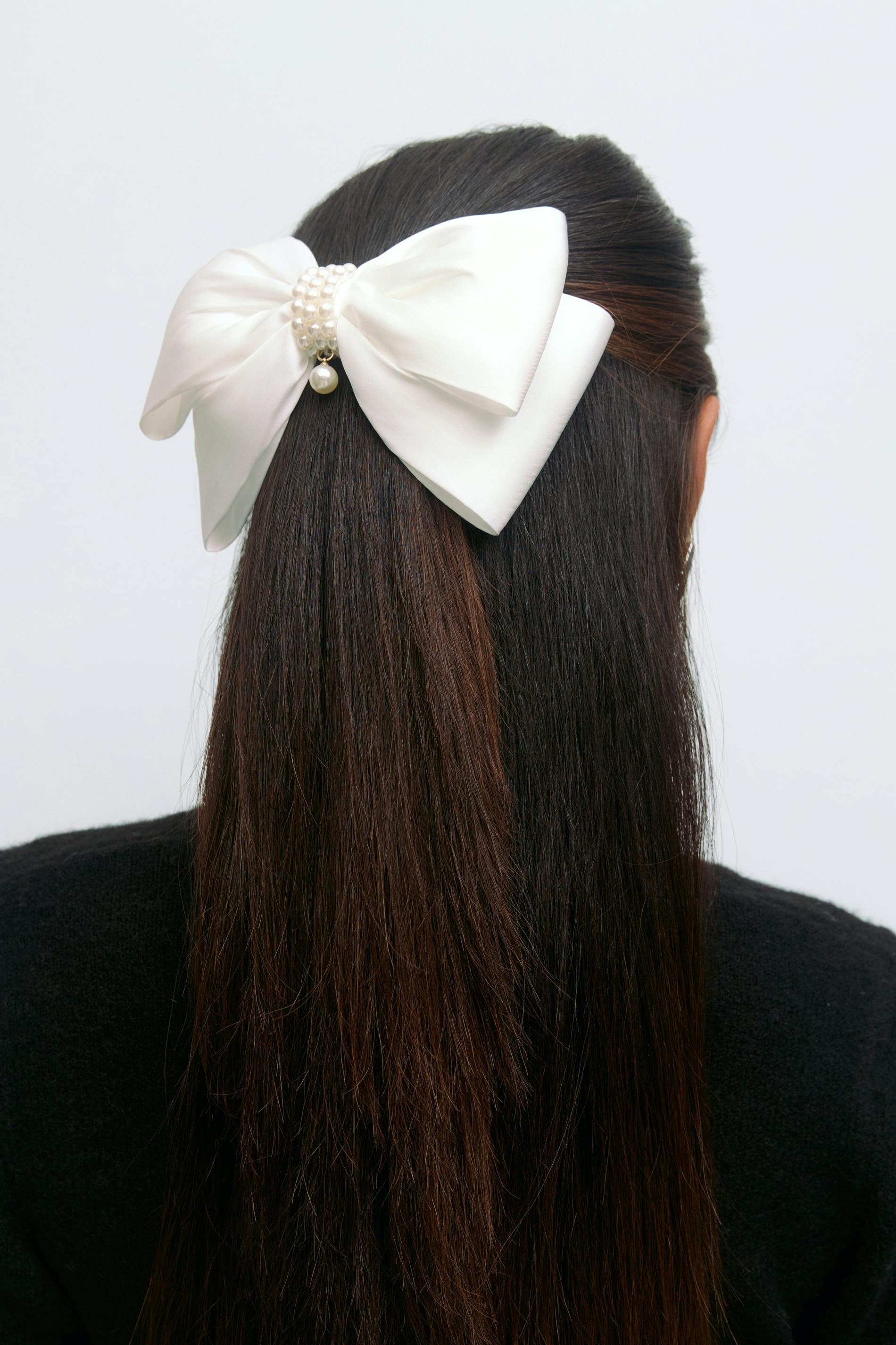 White satin bow hair clip embellished with a clustered pearl center and a single dangling pearl, styled with a black sweater.