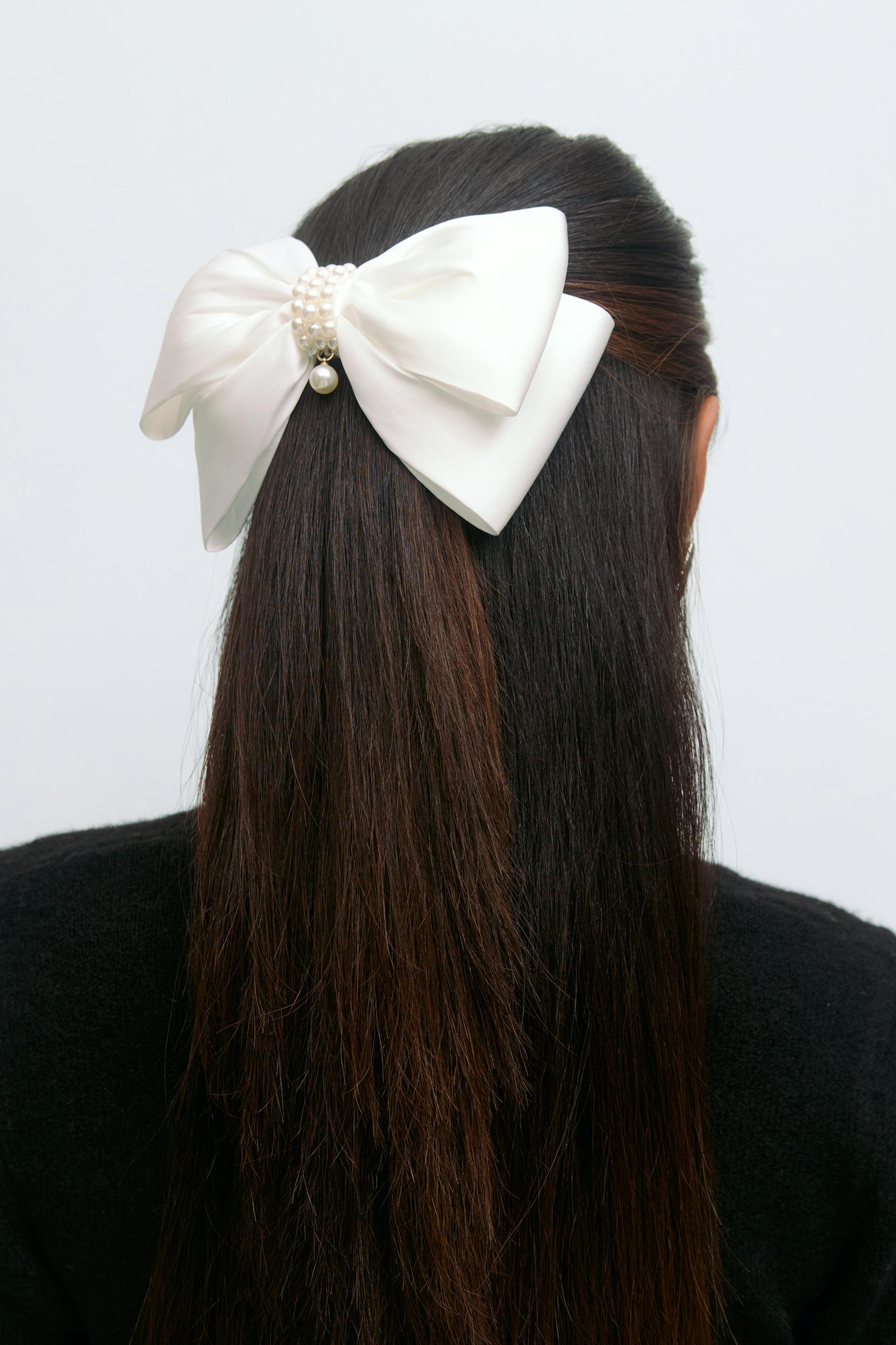 White satin bow hair clip embellished with a clustered pearl center and a single dangling pearl, styled with a black sweater.