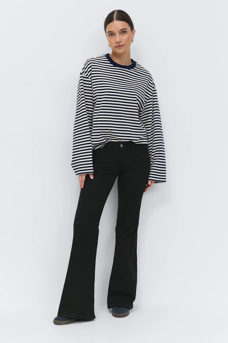 Langærmet, horisontalstripet topp med rund hals i marineblå og hvite striper i en avslappet passform, kombinert med svarte jeans og mørke fritidssko.