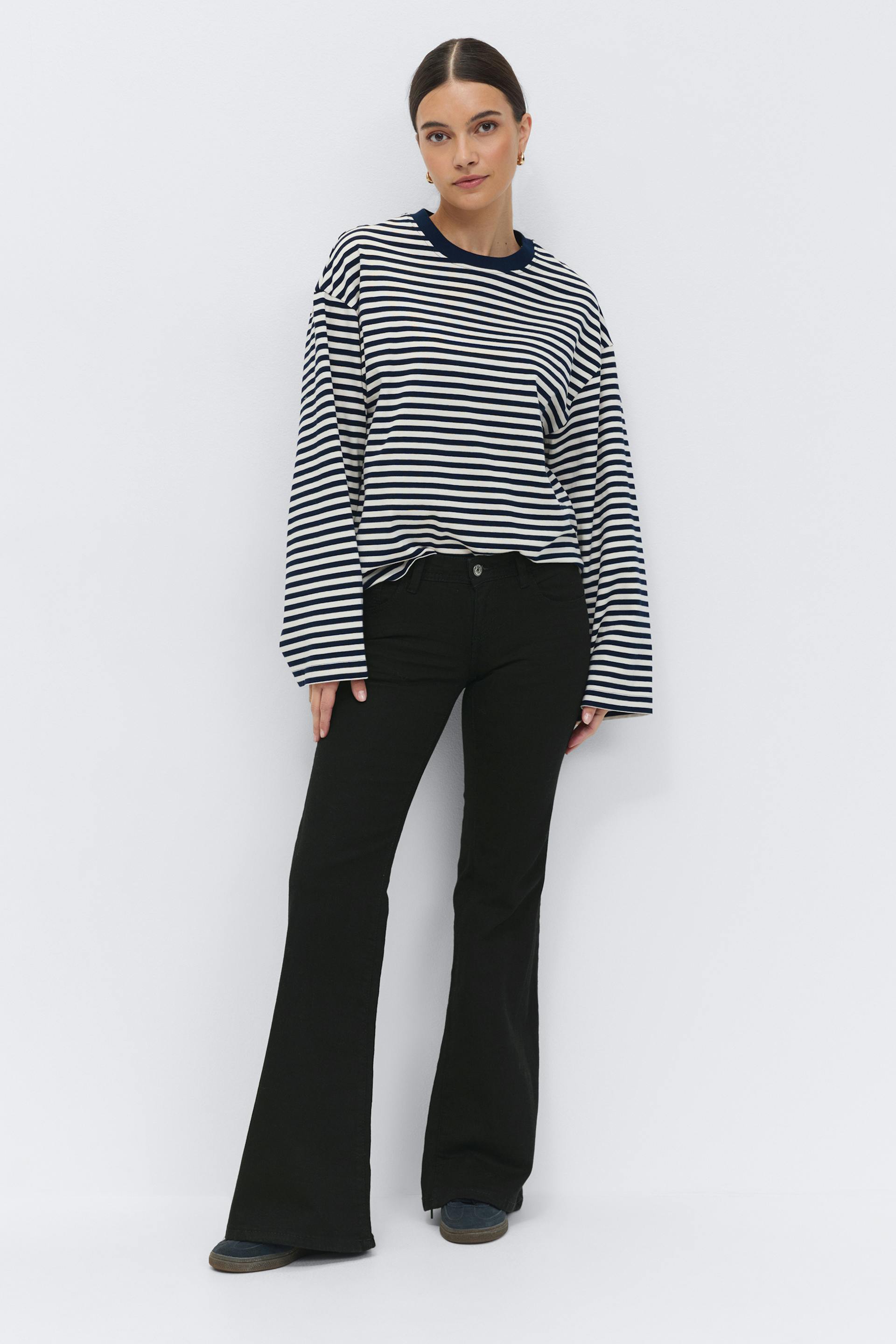 Navy-and-white horizontal striped long-sleeve crewneck top in a relaxed fit, paired with black mid-rise flared jeans and dark casual shoes.