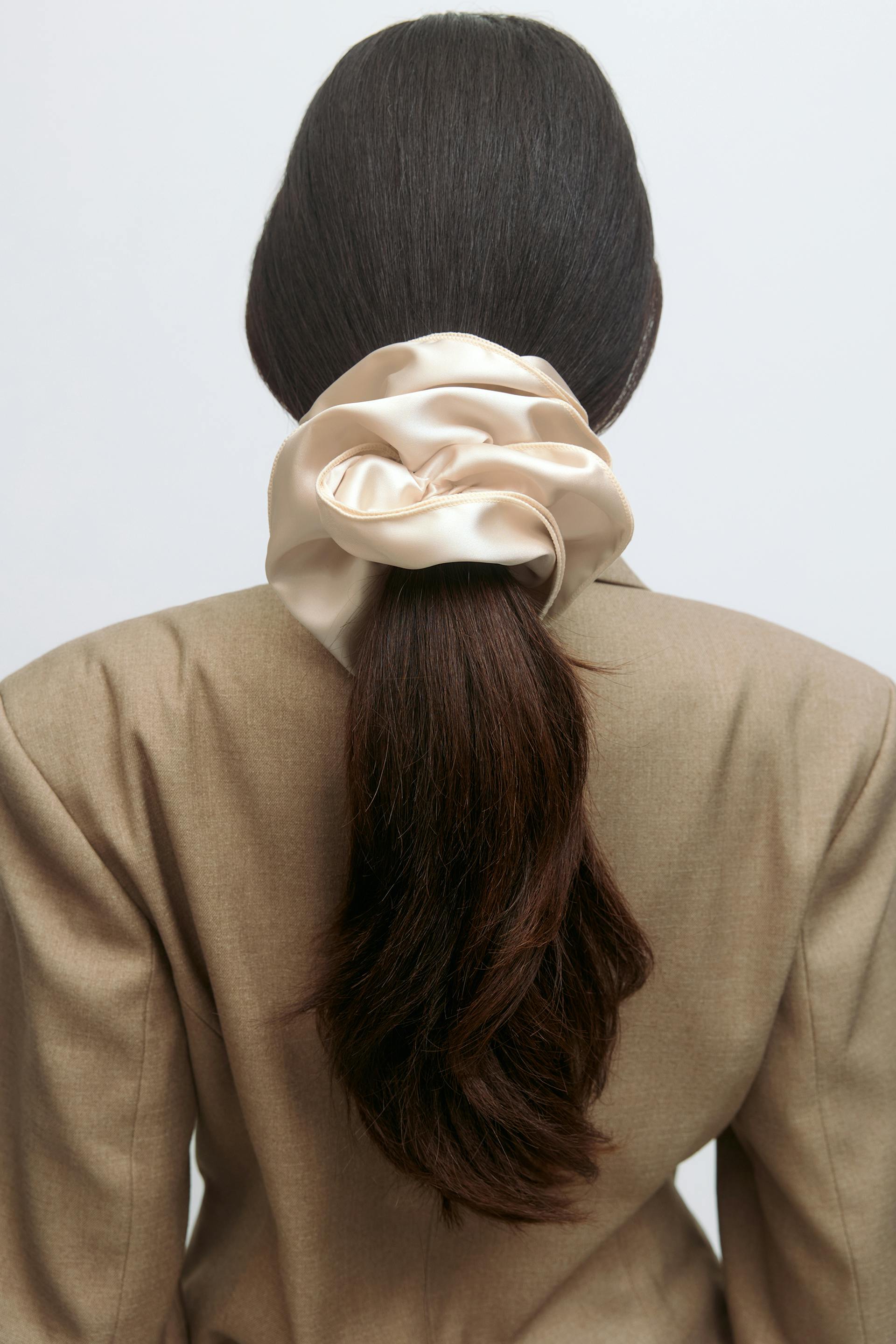 Beige tailored blazer paired with an oversized cream satin scrunchie securing a low ponytail.