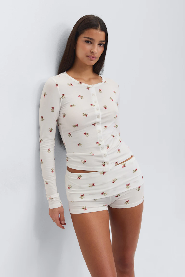 Vit figurnära långärmad topp med rund halsringning och små röda blommor, kombinerad med matchande vita figurnära shorts i samma blommönster.