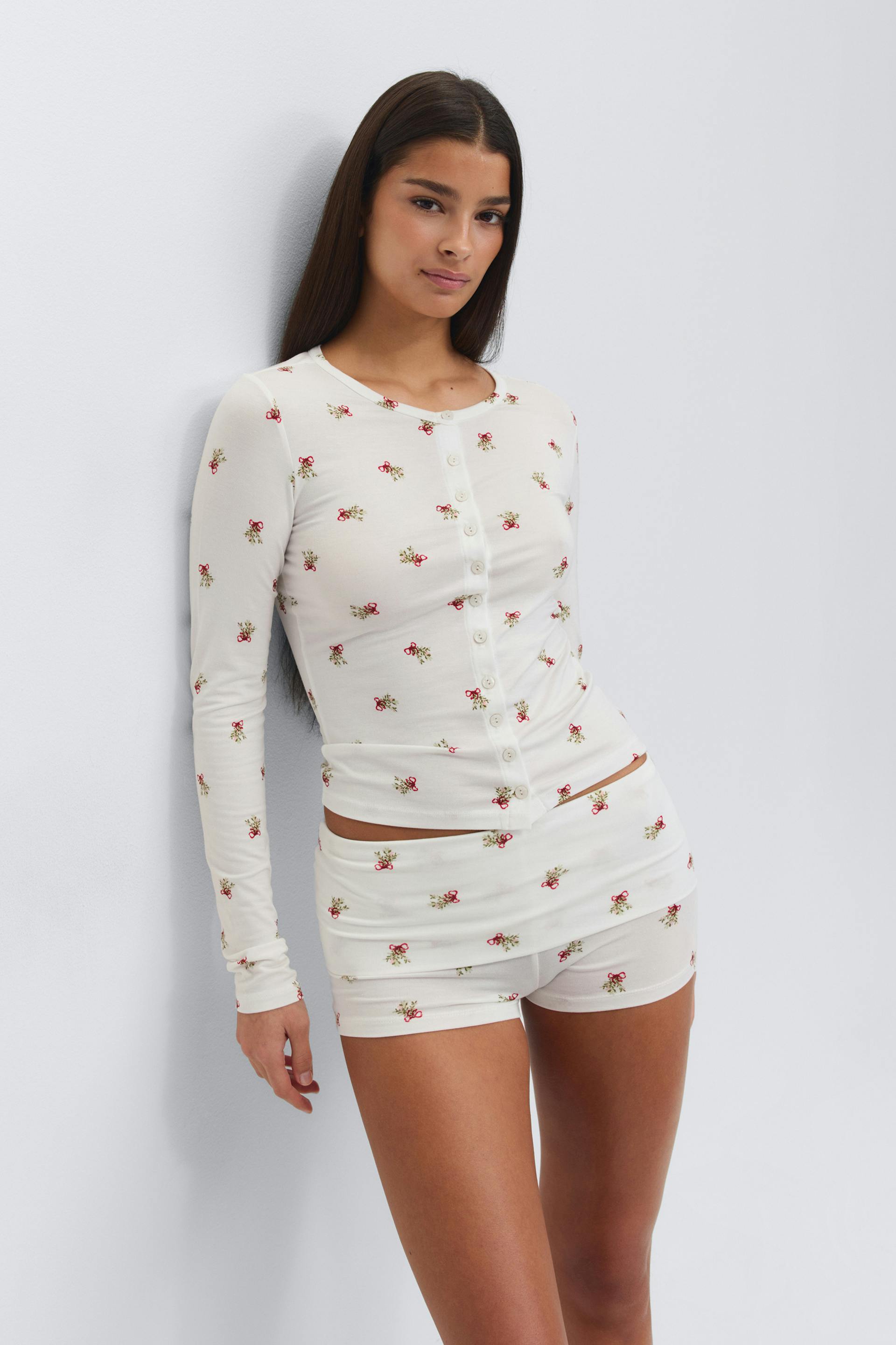 Vit figurnära långärmad topp med rund halsringning och små röda blommor, kombinerad med matchande vita figurnära shorts i samma blommönster.