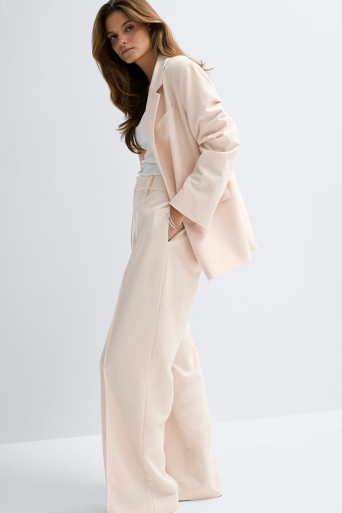 Blazer de tailleur blond pâle à revers cranté porté sur un débardeur blanc, associé à un pantalon large à taille haute assorti.