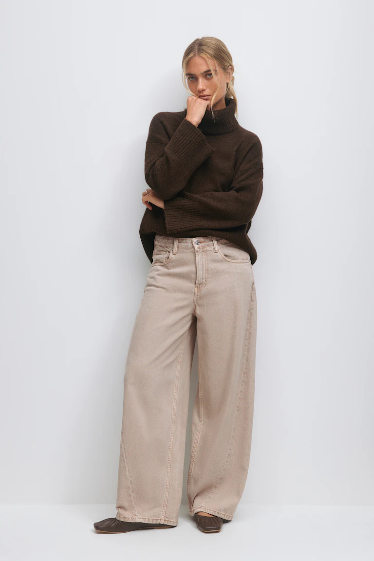 Mørkebrun, oversized turtleneck-genser med ribbestrikkede mansjetter, sammen med beige jeans med høy midje og brune flate sko med firkantet tå.