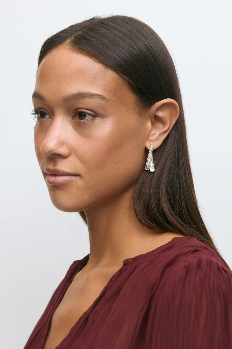 Long-sleeve burgundy textured V-neck blouse paired with silver-tone drop earrings set with multiple clear faceted stones.