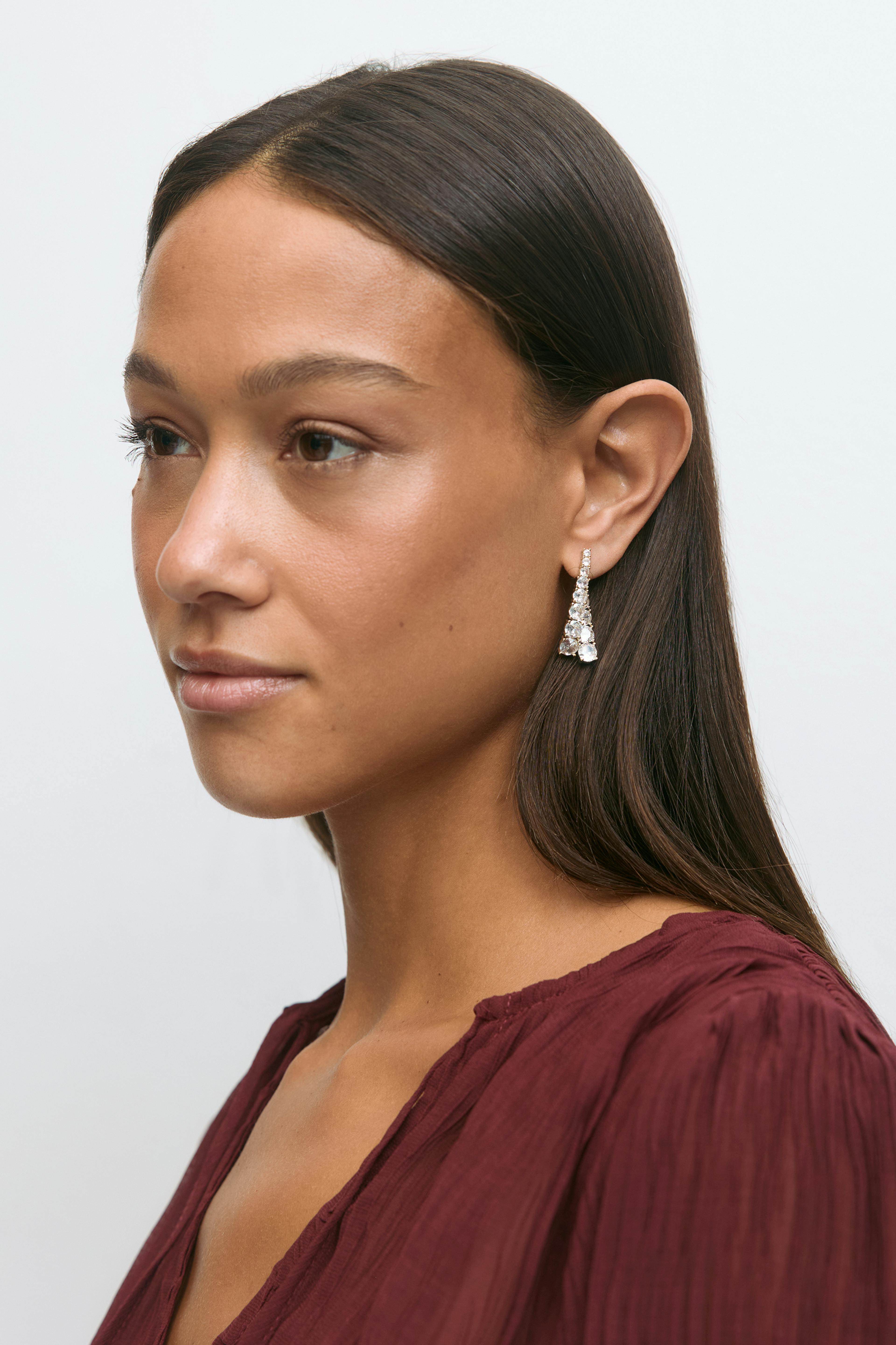 Chemisier à manches longues à col en V texturé bordeaux associé à des boucles d'oreilles en argent serties de multiples pierres claires à facettes.