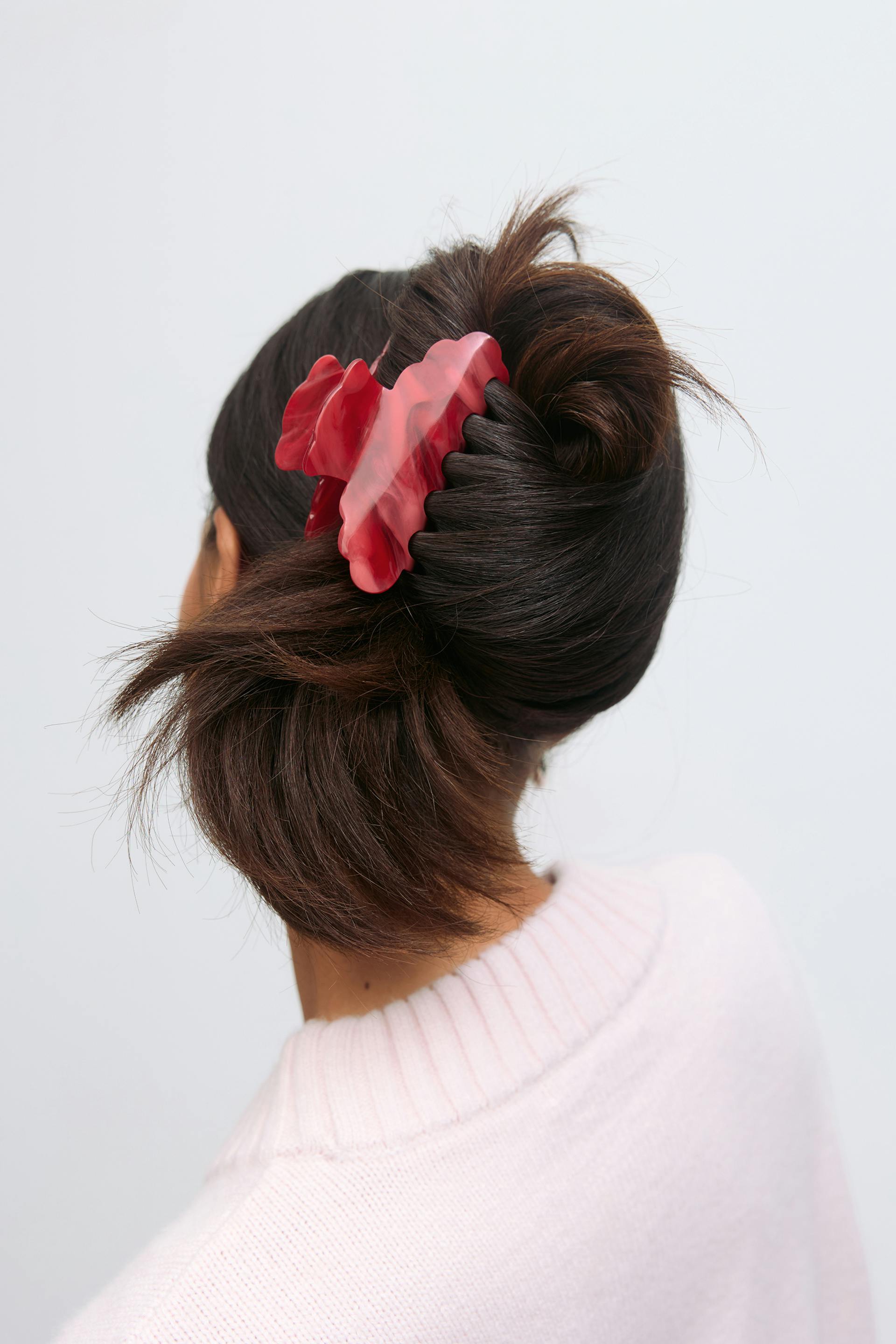 Light-pink ribbed crewneck sweater and a large red marbled hair claw clip.