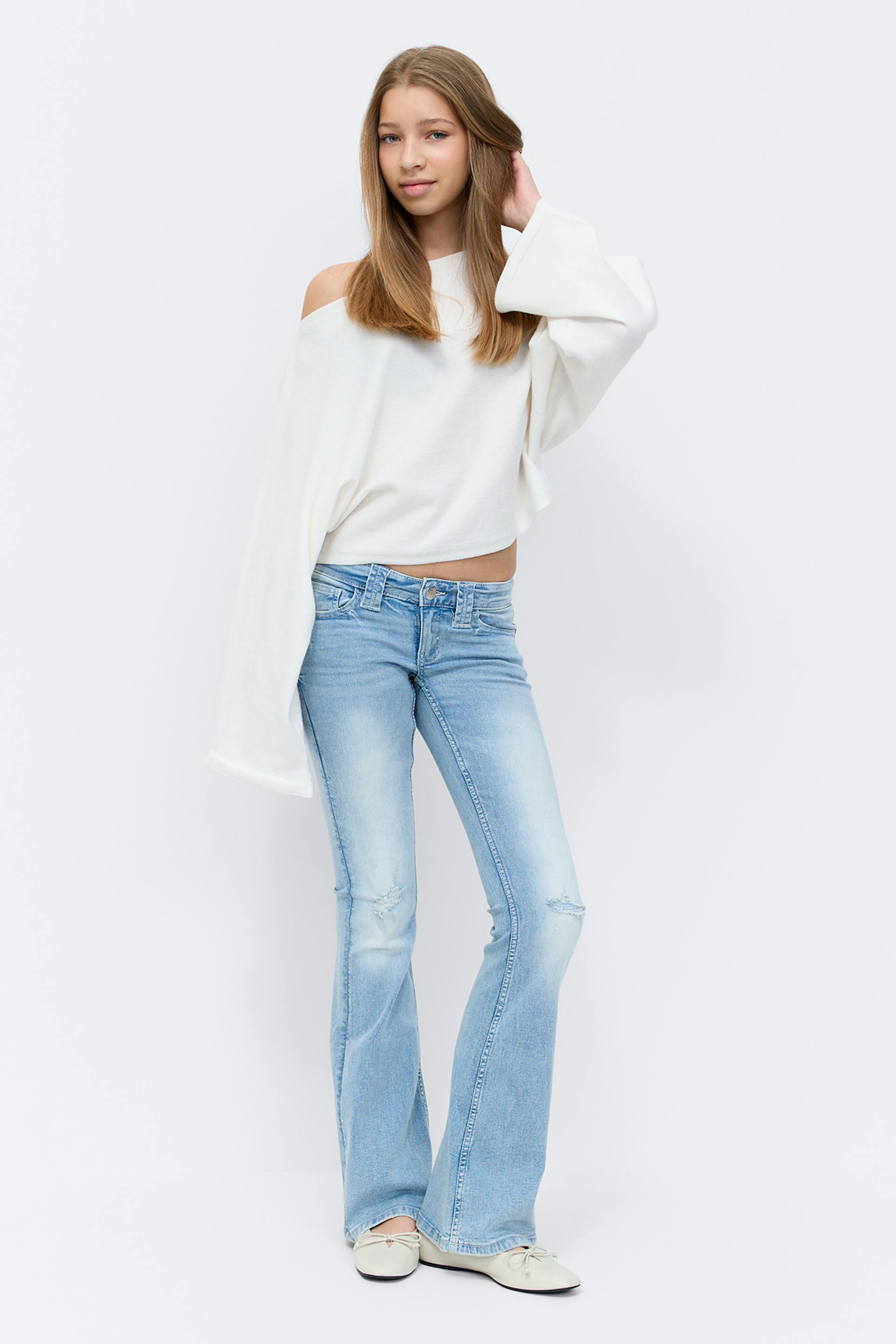 Back view of a model wearing an ivory cropped knit sweater paired with light‑wash skinny jeans and a silver bracelet.