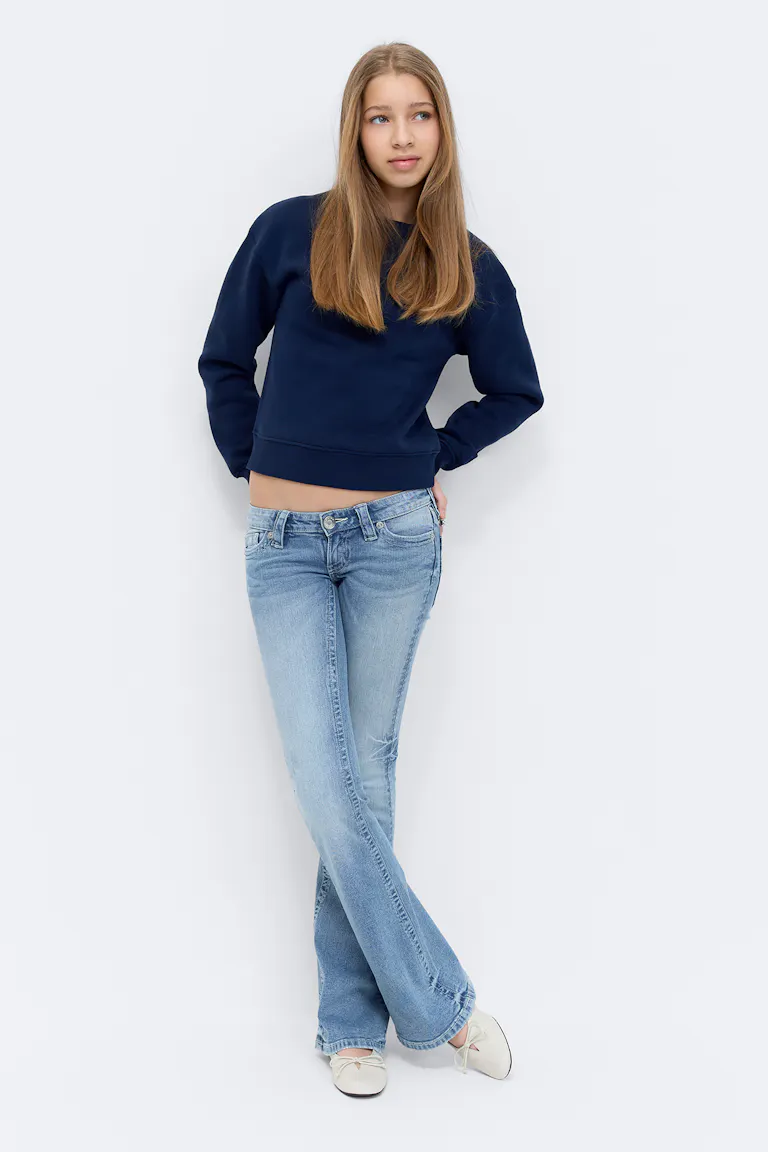 Navy crewneck sweatshirt, light-wash low-rise bootcut jeans, and cream ballet flats with small bows.