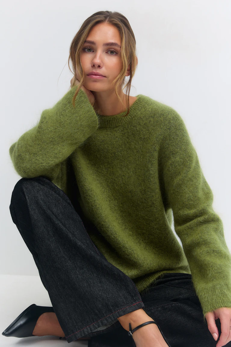 Pull à col roulé flou vert olive, jean noir à jambe large et talons noirs à bout pointu.