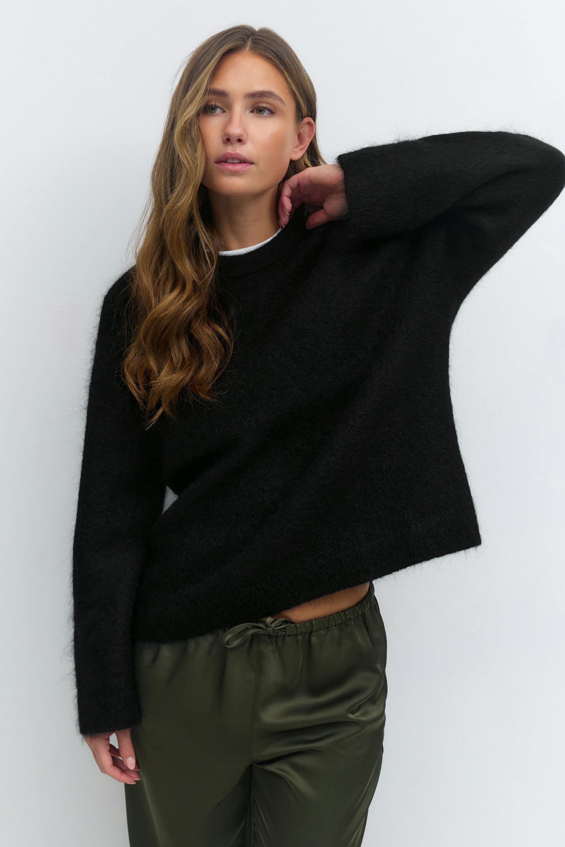 Schwarzer langärmeliger Pullover mit wuscheligem Rundhalsausschnitt über einem weißen T-Shirt mit Rundhalsausschnitt, gepaart mit einer olivgrünen Satinhose mit Kordelzug.