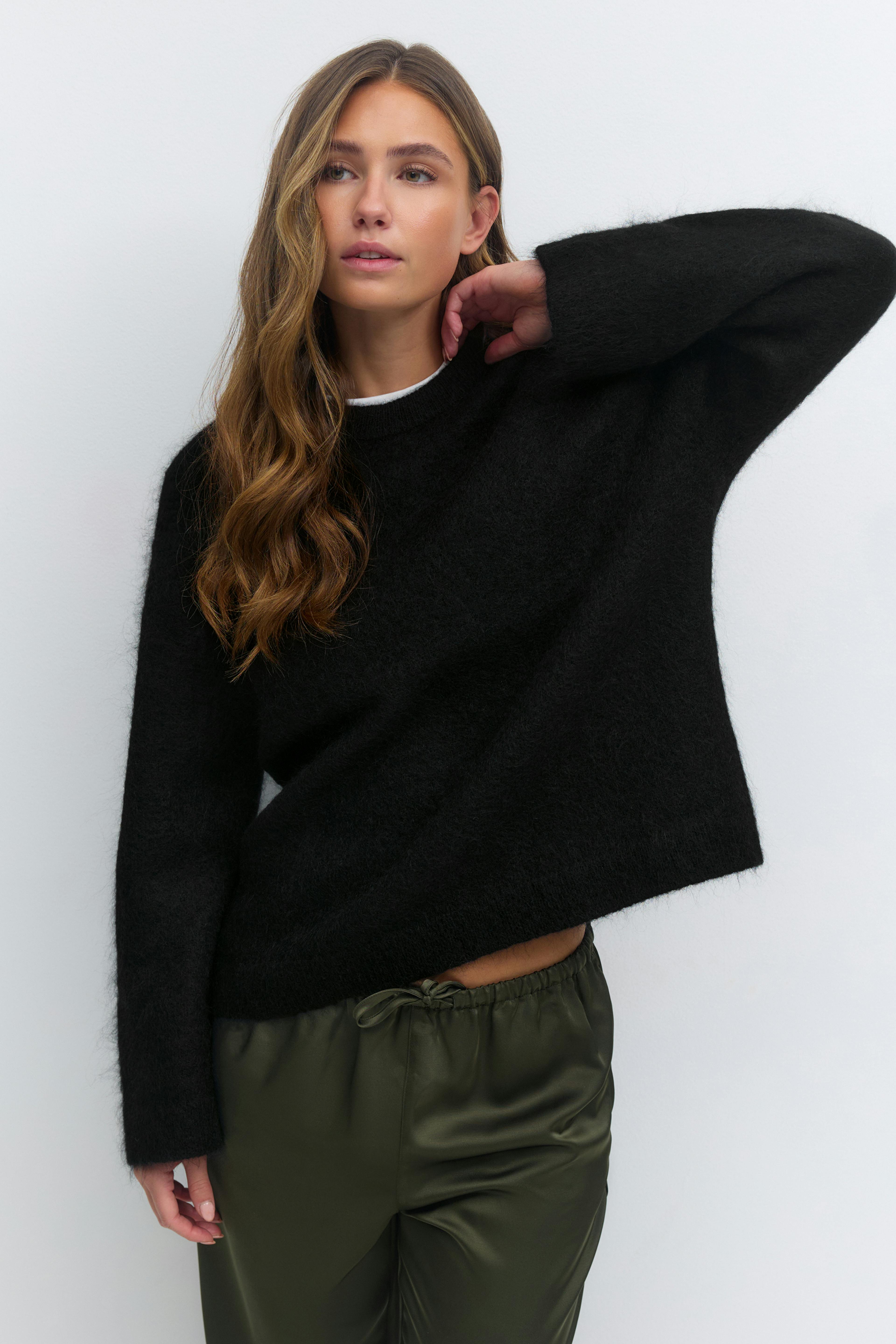 Pull noir à manches longues et col ras du cou, superposé à un tee-shirt blanc à col ras du cou, associé à un pantalon à cordon en satin vert olive.