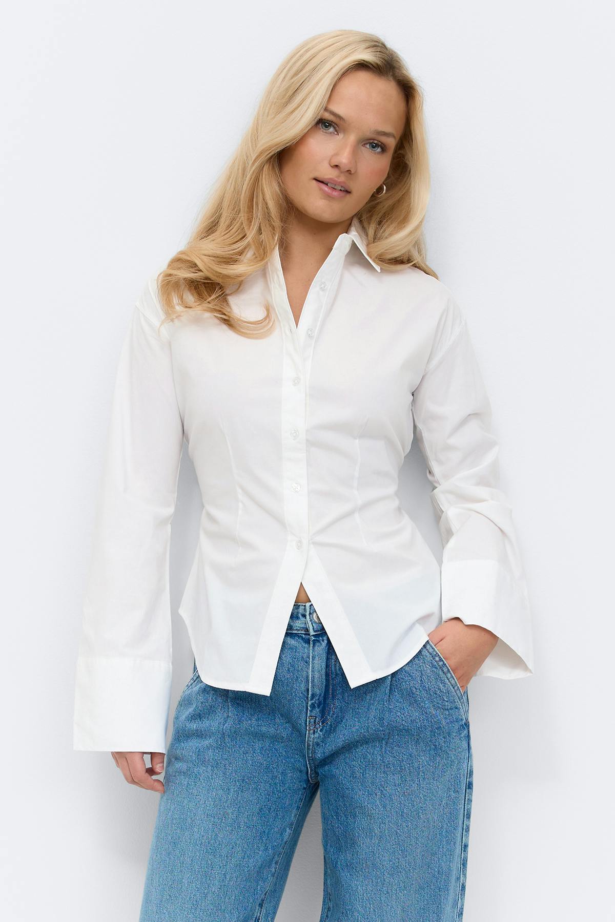 White long-sleeve button-down shirt with wide cuffs and a subtle waist tie, paired with black wide-leg trousers, white socks and black loafers.