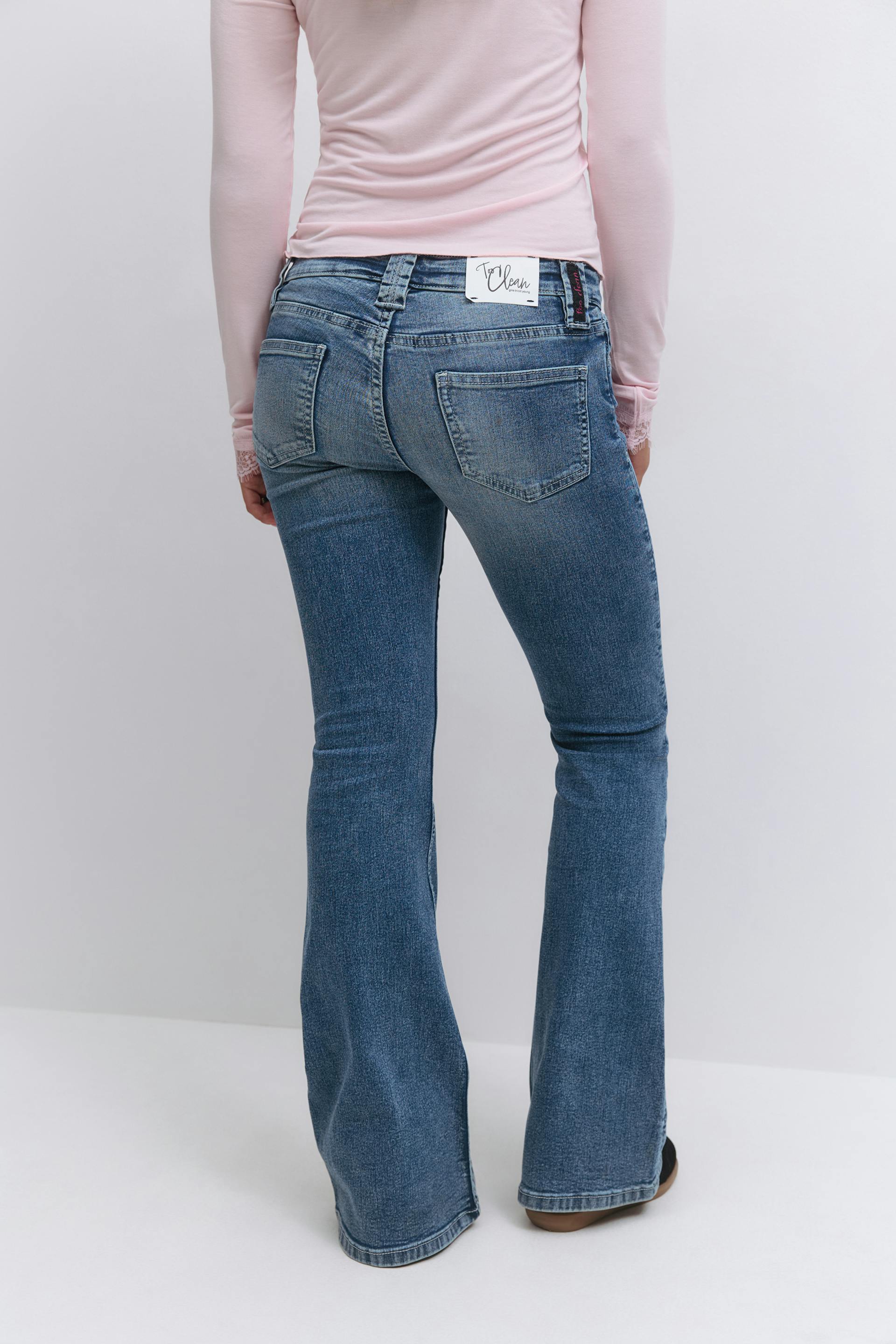 Light pink long-sleeve top tucked into medium-wash bootcut jeans with rear patch pockets and subtle fading.
