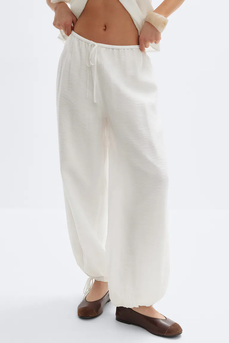 Cream-white drawstring wide-leg trousers with elasticated tie ankles, paired with brown leather ballet flats with darker toe caps.