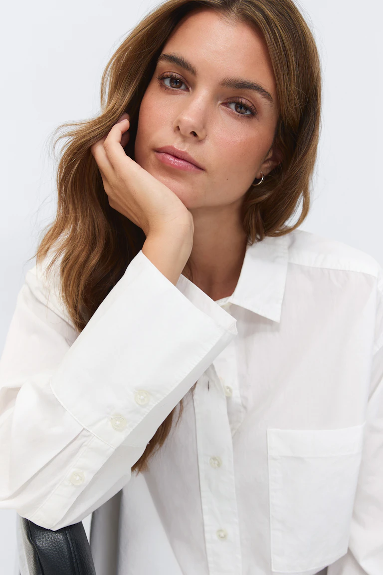 Chemise blanche surdimensionnée à manches longues et à poches sur la poitrine, associée à un jean droit haut délavé et à de petites boucles d'oreilles dorées.