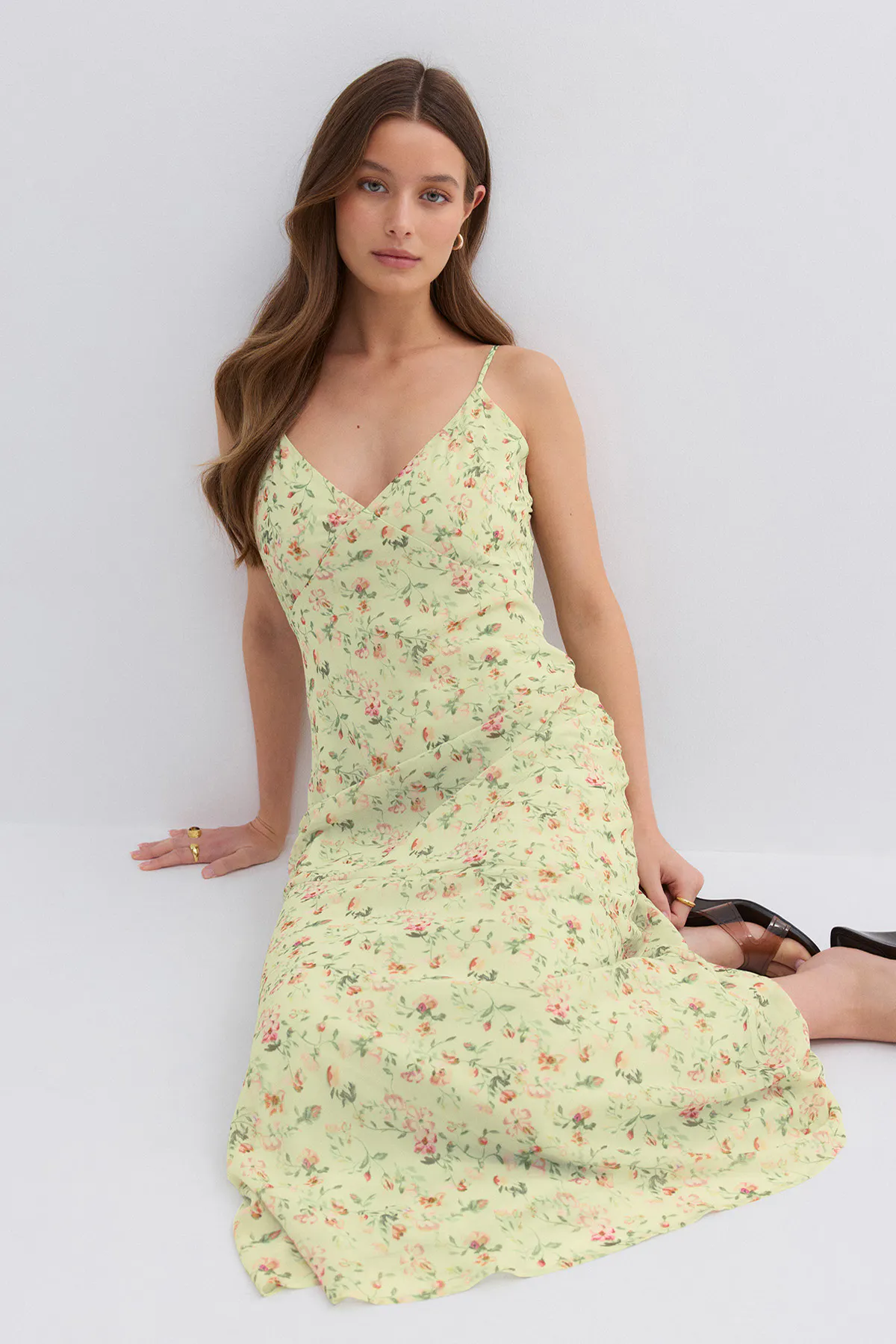 Lysegrønn maxikjole med blomstermønster, tynne spaghettistropper og V-utringning, stylet med øreringer i gull, gullringer og brune sandaler med hæl.