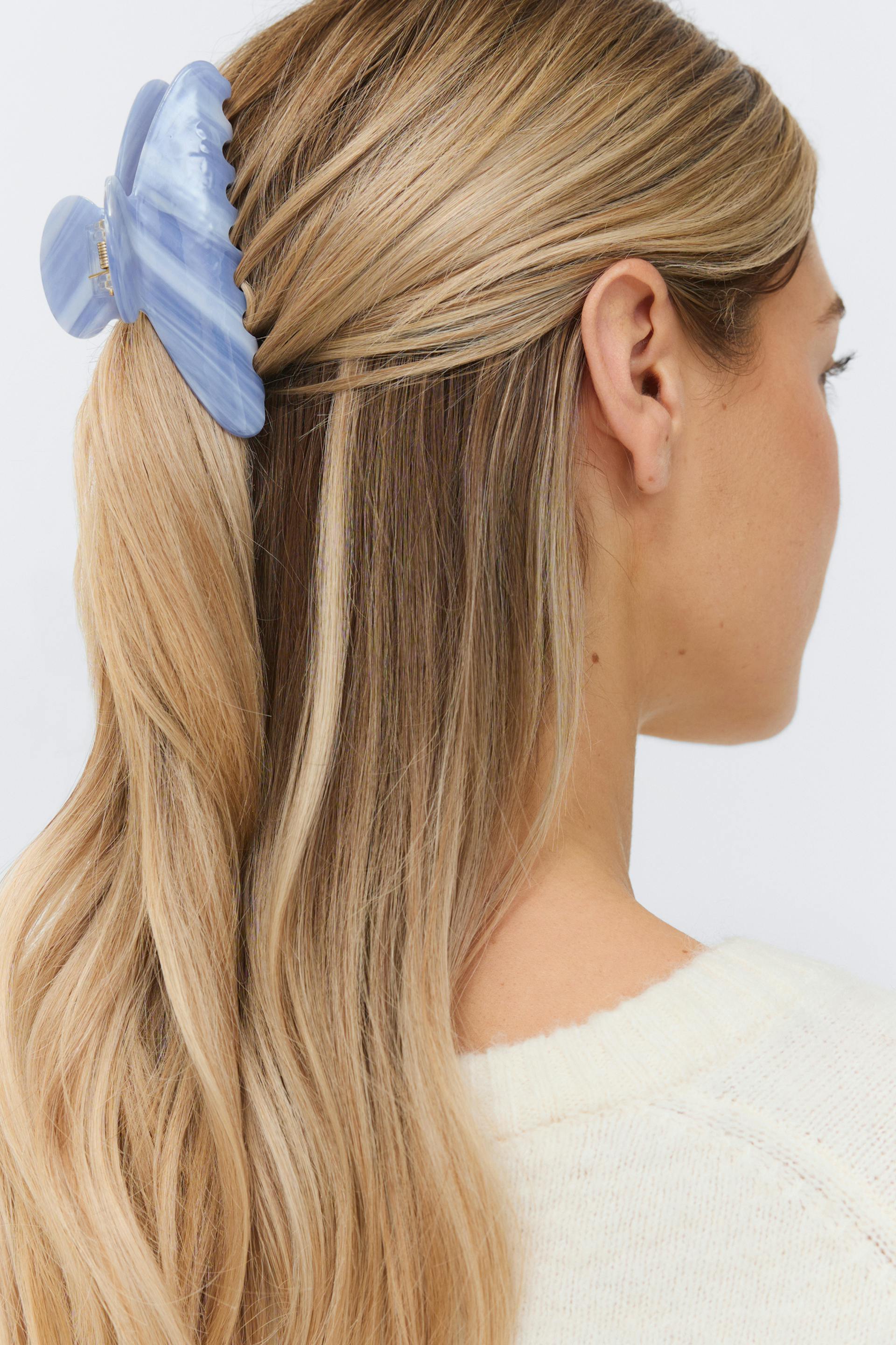 Off-white knit sweater and a large marbled light-blue hair claw clip securing a half-up hairstyle.
