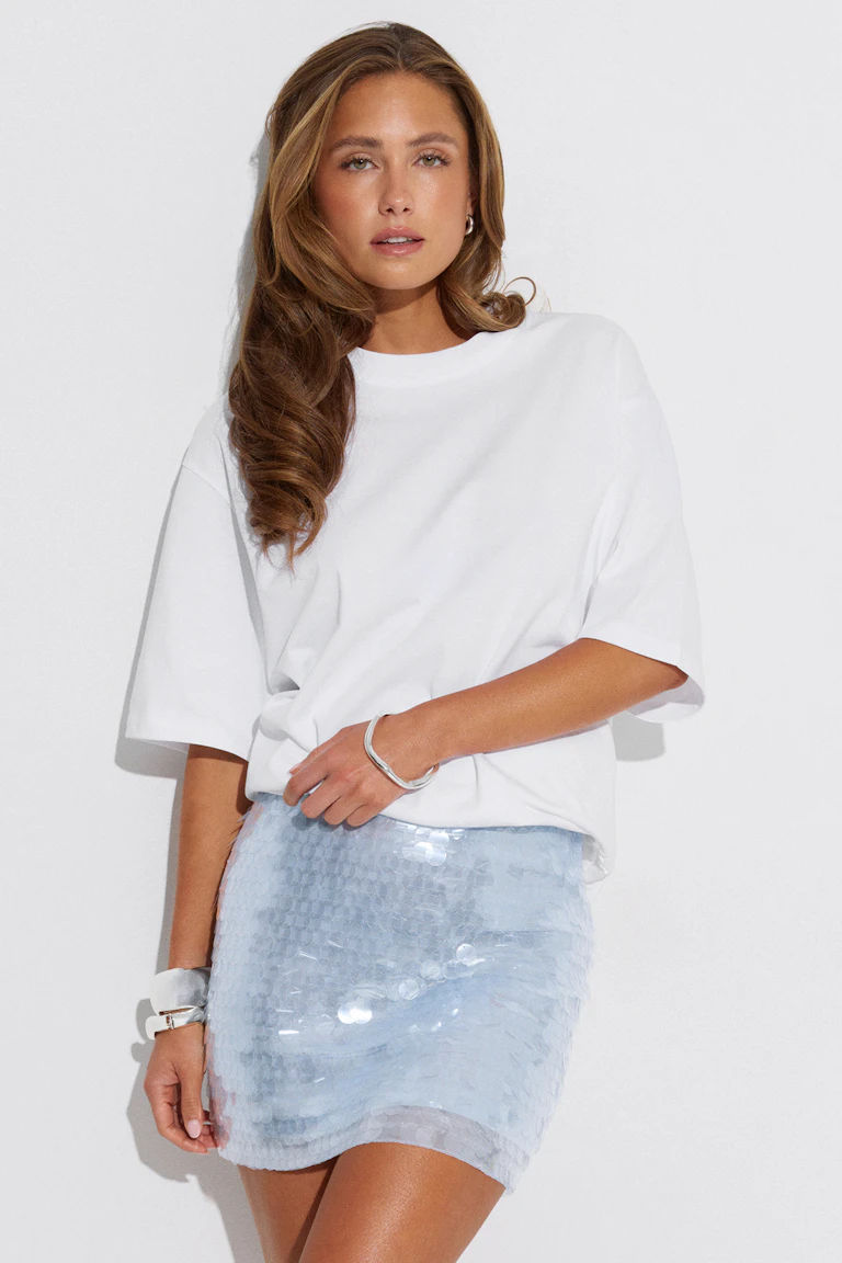 Hvid oversized kortærmet T-shirt sat sammen med en lyseblå pailletbesat mininederdel; suppleret med et sølvarmbånd, et hvidt manchetarmbånd og en lille ørering.