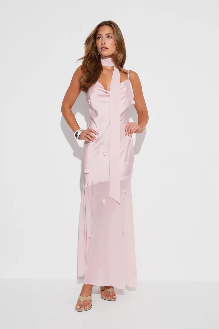 Zartrosa Maxikleid aus Satin mit Kuttenausschnitt und dünnen Trägern, langem, passendem Halstuch, verstreuten Blumenapplikationen und durchscheinendem Unterrock; kombiniert mit beigen, offenen Sandalen und einem silbernen Armreif.