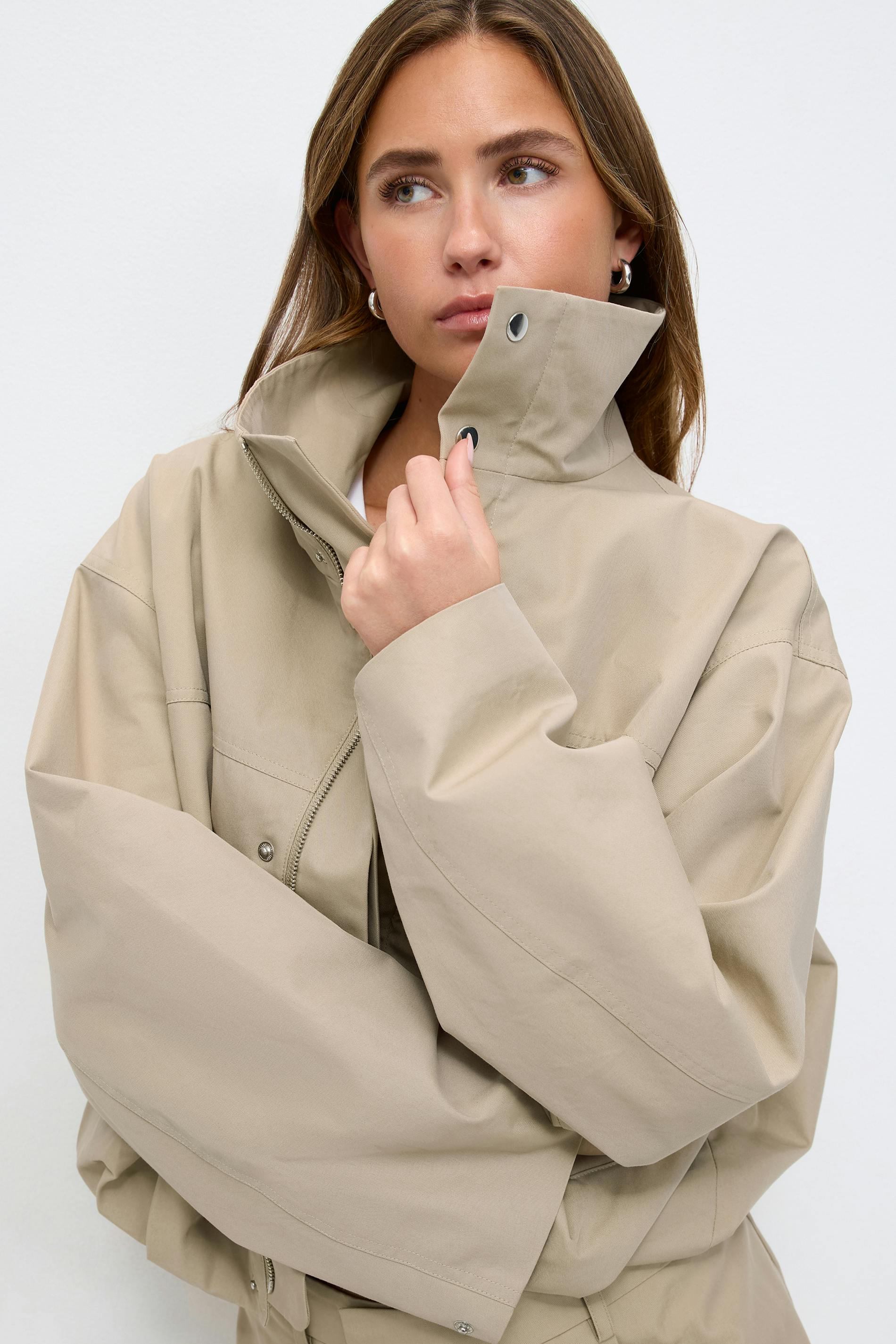 Beige oversized zip-front jacket with high stand collar and snap-button placket, long voluminous sleeves, paired with matching beige trousers.
