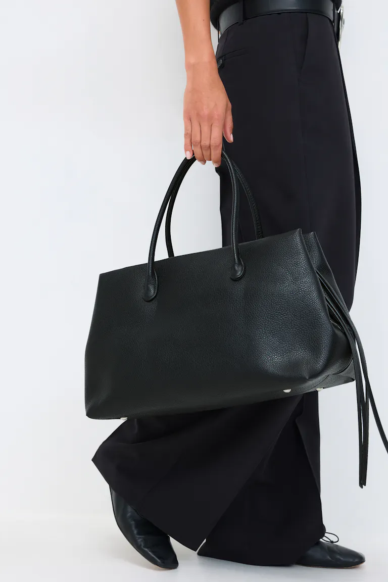 Een zwarte broek met wijde pijpen en een zwarte leren riem, gecombineerd met zwarte leren pumps met puntige teen en een grote zwarte leren tas met dubbele bovenhengsels en kwastjes.