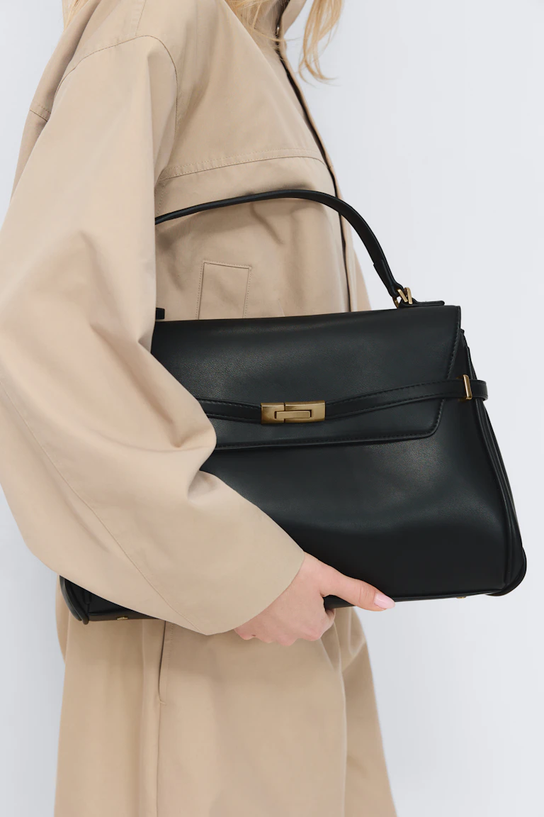 Beige trenchcoat tillsammans med en svart läderväska med topphandtag och guldfärgad hårdvara.