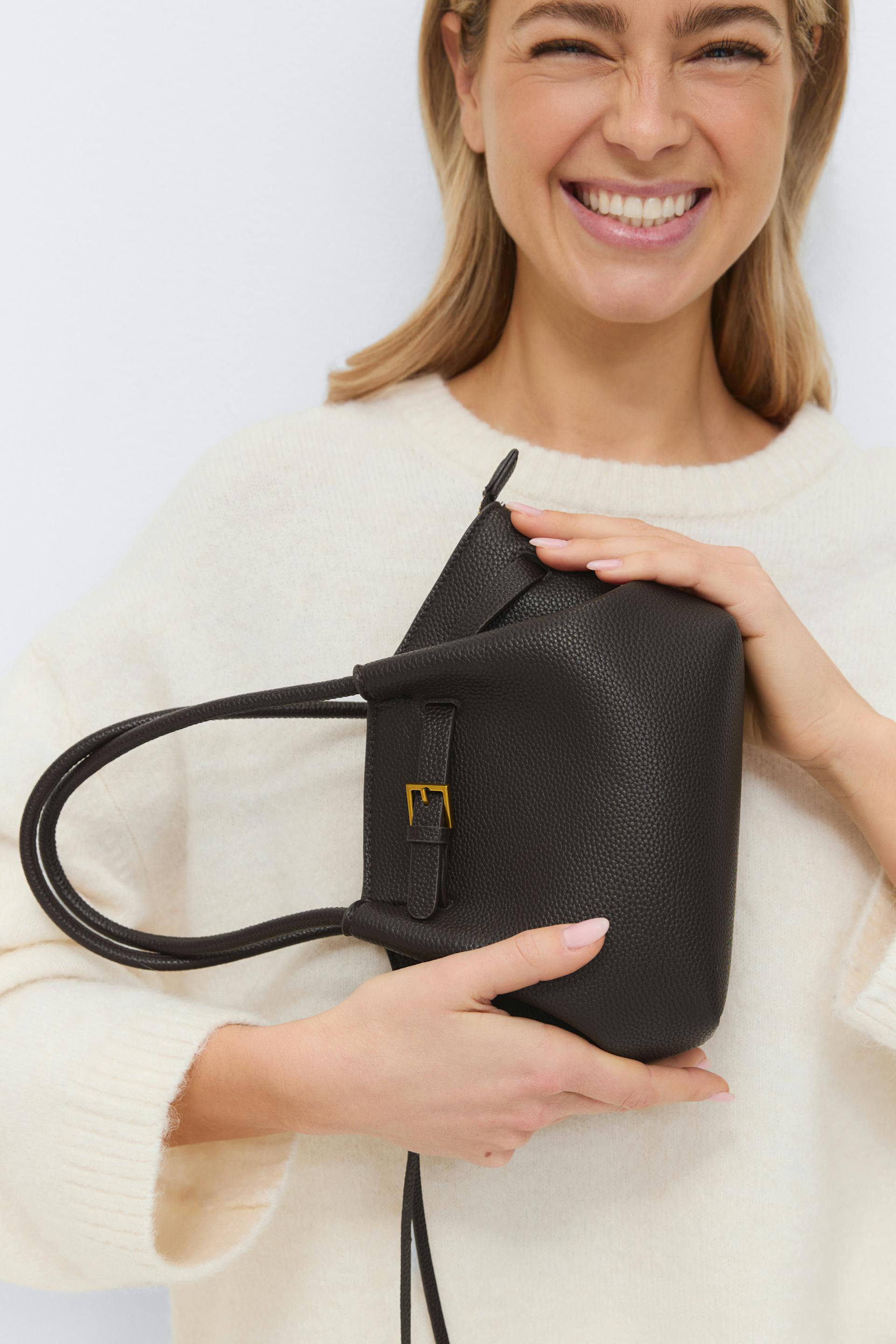 Cream crewneck knit sweater paired with a dark brown pebbled leather top-handle bag featuring a gold buckle detail.