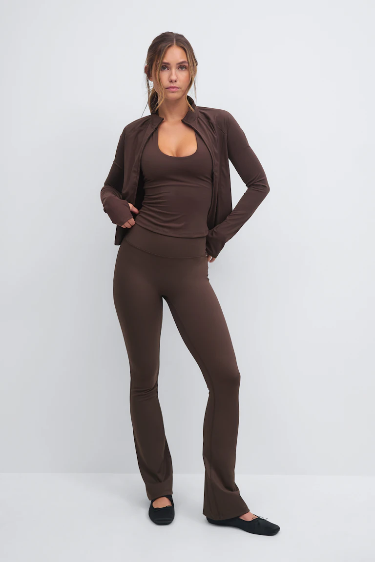 Veste zippée ajustée marron chocolat sur un débardeur à encolure dégagée assorti, associé à un legging évasé taille haute et à des ballerines noires.