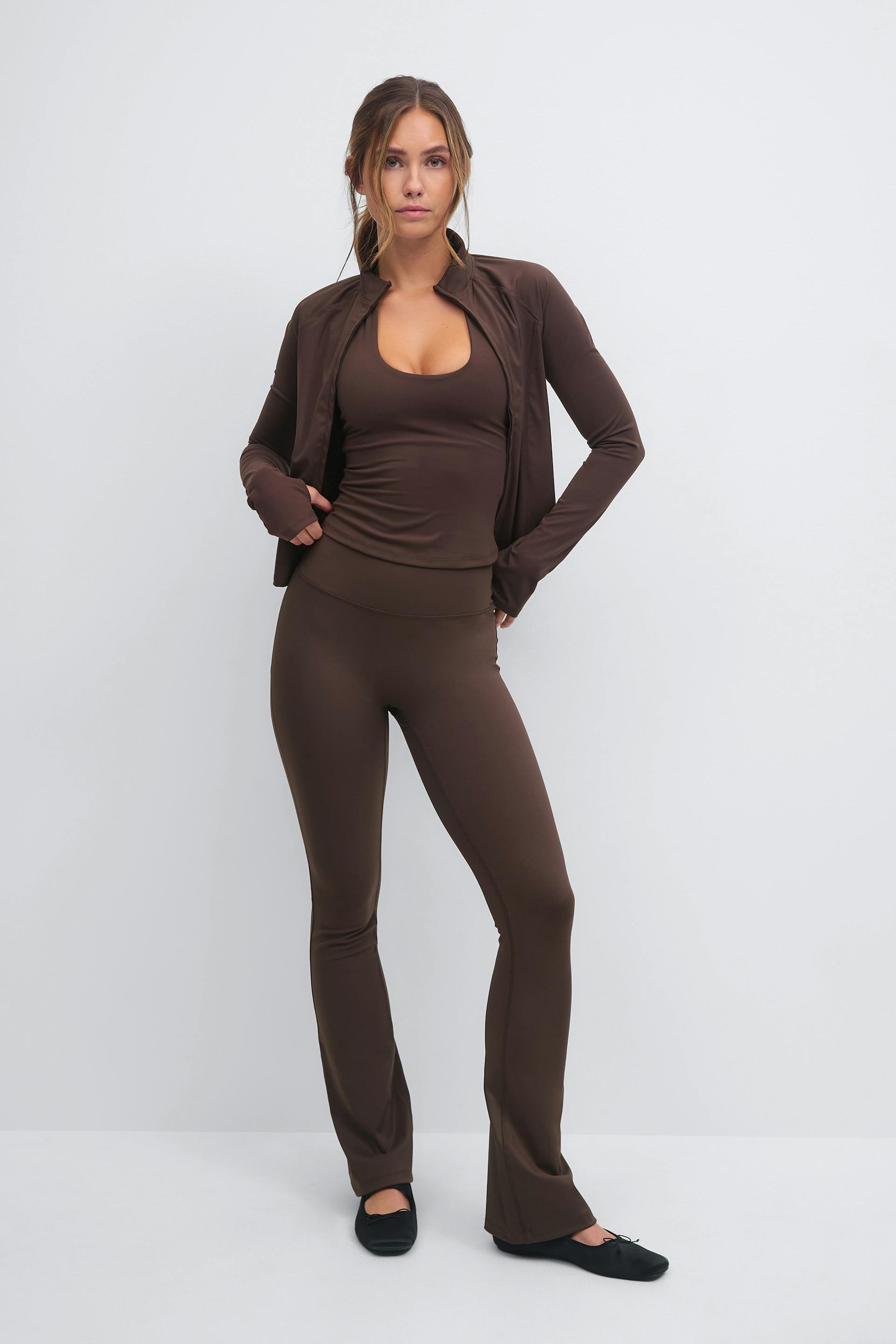 Chocolate-brown fitted zip-up jacket over a matching scoop-neck tank, paired with high-waist flared leggings and black ballet flats.
