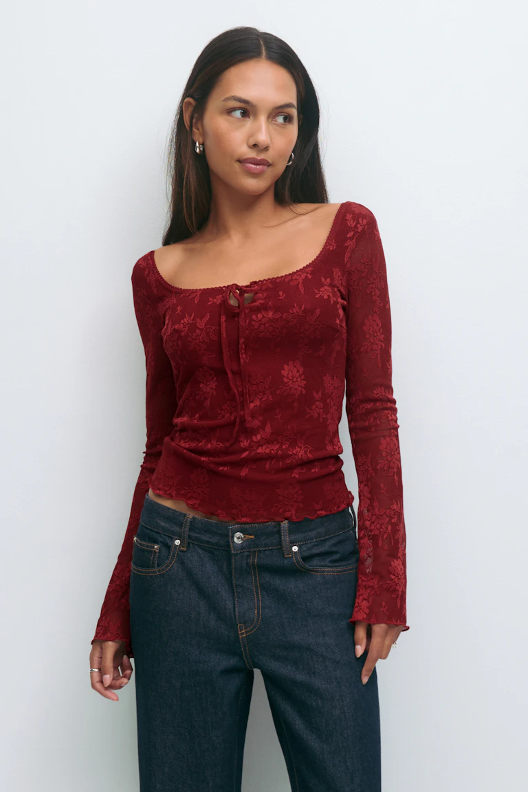 Deep red long-sleeve floral jacquard fitted top with square scoop neckline, front tie detail and lettuce hem, paired with dark indigo straight-leg jeans with contrast stitching.