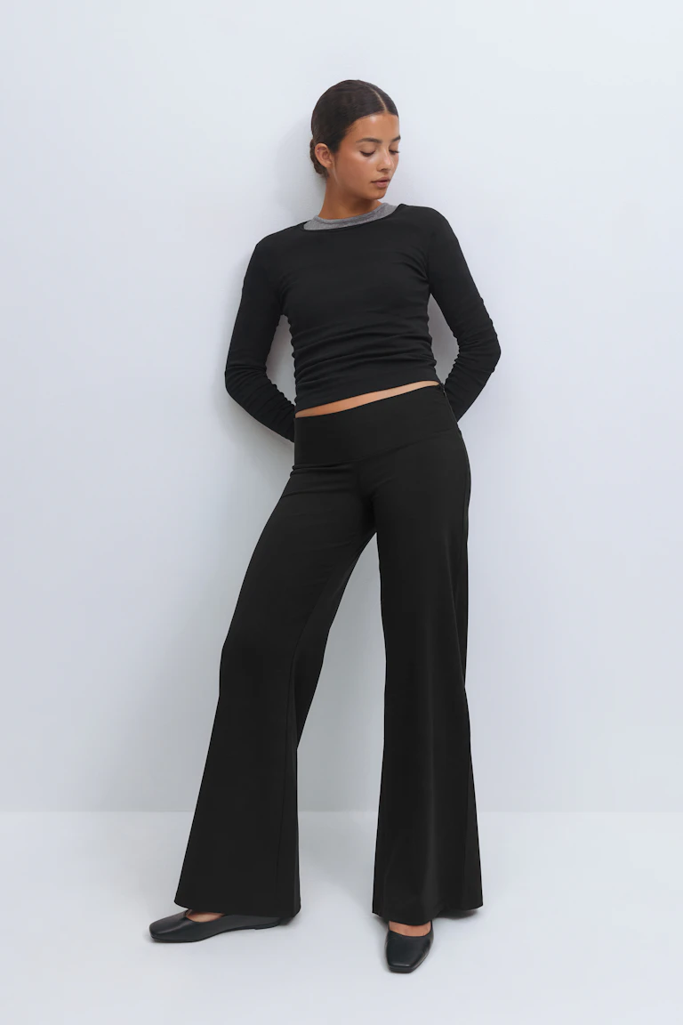 Zwarte getailleerde top met lange mouwen en een zichtbare grijze crew-neck onderlaag, gecombineerd met een zwarte wijde broek met hoge taille en zwarte ballerina's met vierkante teen.