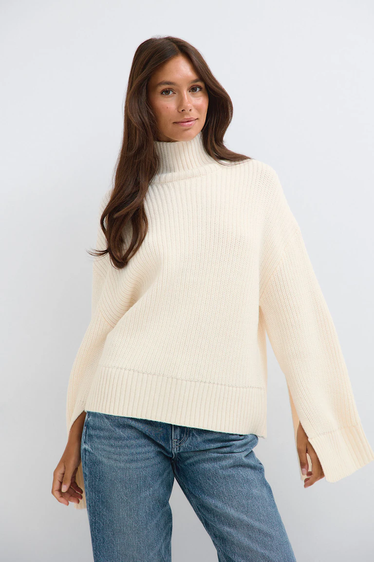 Cremefarbener, gerippter Rollkragenpullover mit weiten Ärmeln und Bluejeans.