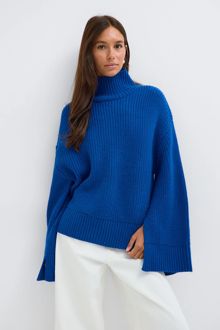 Königsblauer, übergroßer Rollkragenpullover mit einer weißen Hose mit weitem Bein.