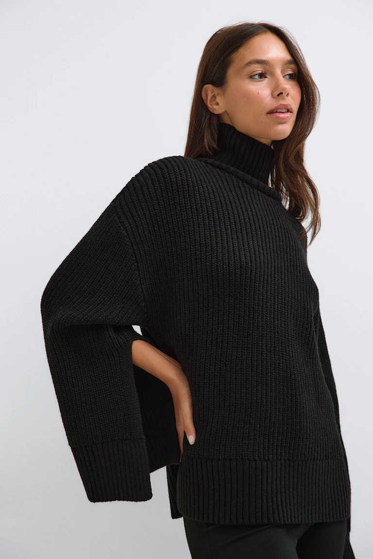 Zwarte, oversized coltrui met ribbelpatroon.