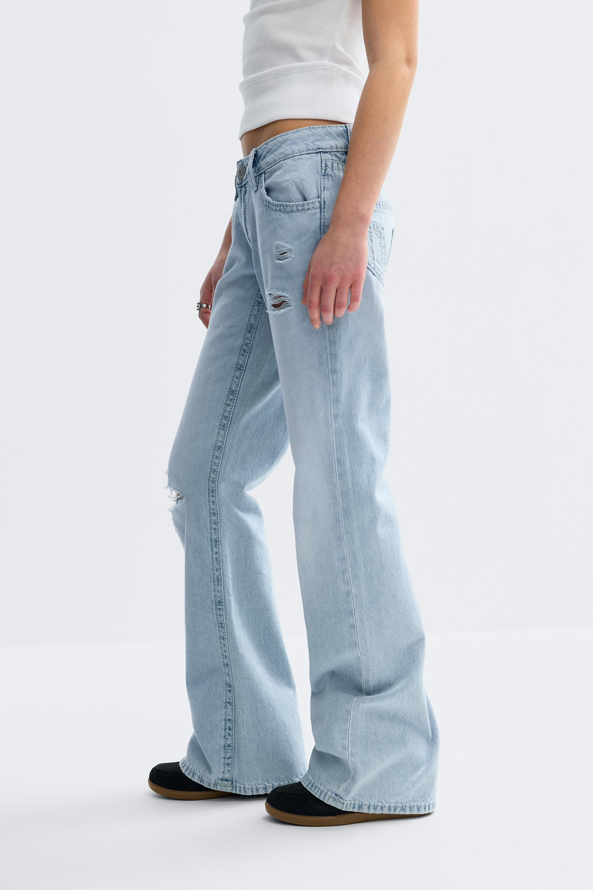 White cropped tank top paired with light‑blue distressed low‑rise wide‑leg jeans and black slip‑on shoes with gum soles.