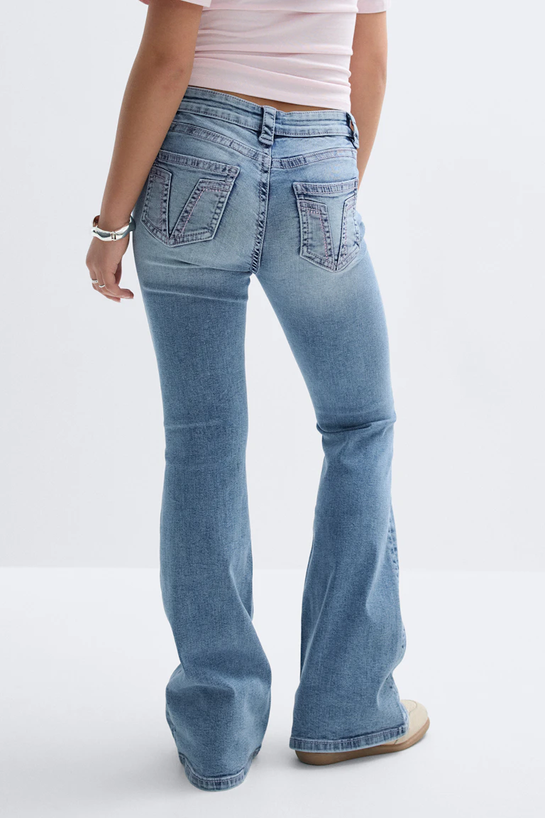 Lichtroze bijgesneden getailleerde top gecombineerd met een lichtgewassen flared jeans met V-gestikte achterzakken, beige sneakers en een zilveren armband.