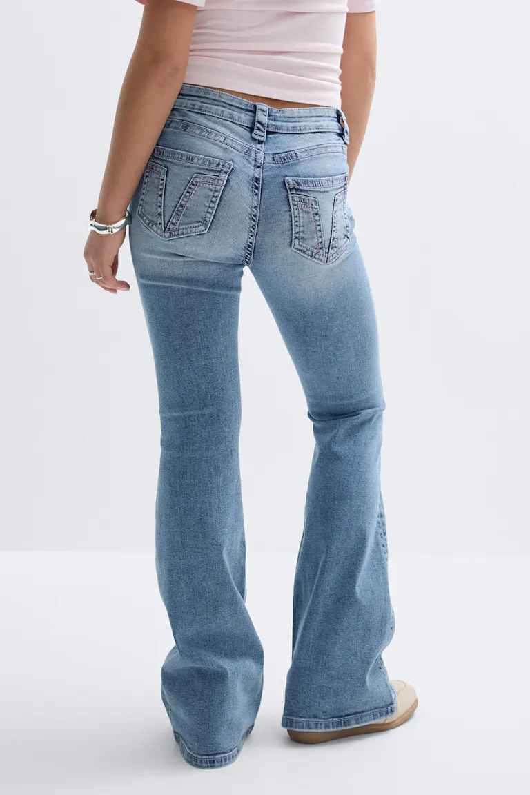 Light pink cropped fitted top paired with light-wash flared jeans with V‑stitched back pockets, beige sneakers and a silver bracelet.