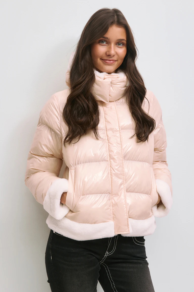 Veste polaire blush brillant avec col entonnoir haut, bordures en fausse fourrure blanche aux poignets et à l'ourlet, et poches latérales ; associée à un jean noir avec surpiqûres contrastées blanches.