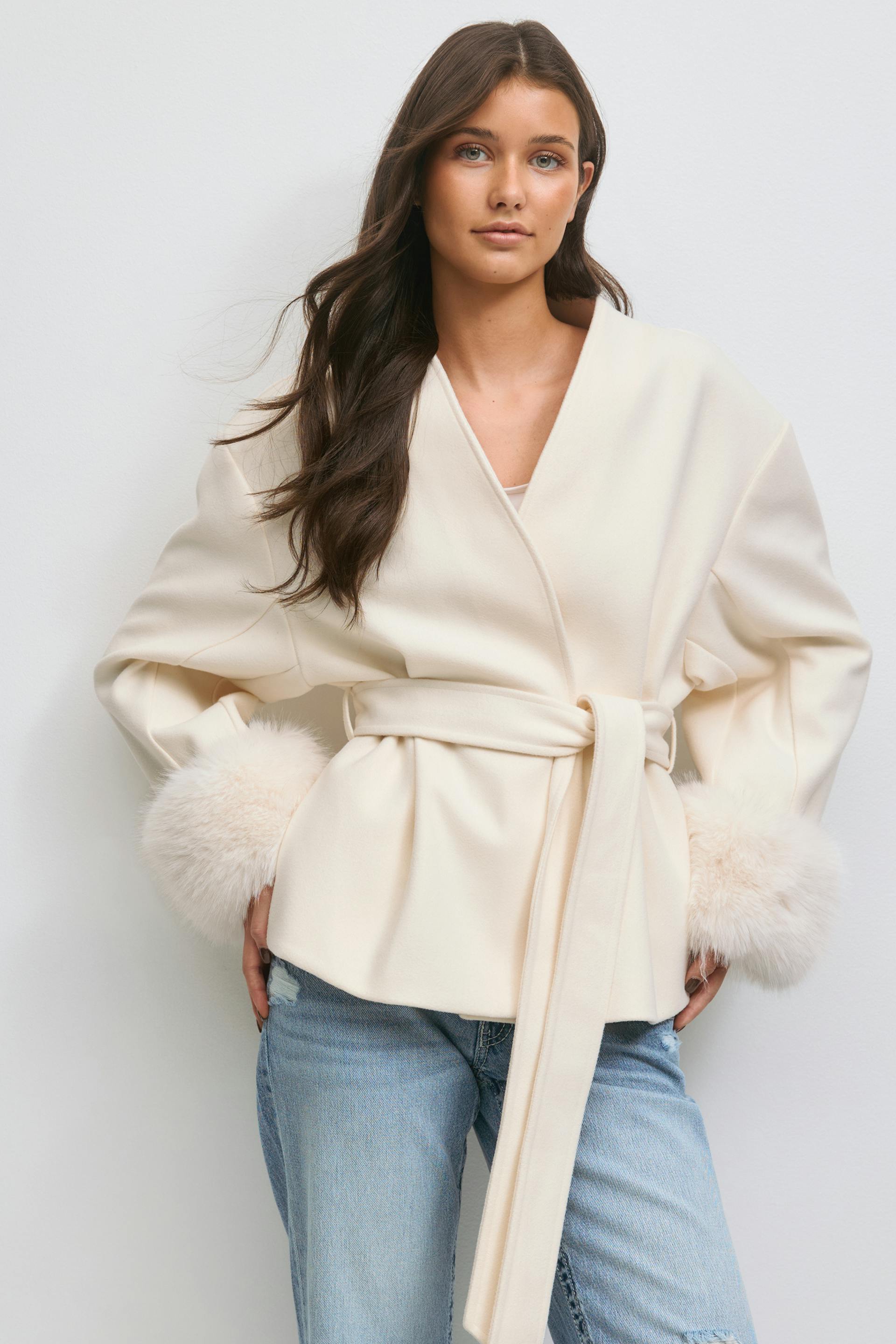 Pehmeän kermanvärinen kietaisutakki, jossa on turkisverhoillut hihansuut, yhdistettynä vaaleanvärisiin distressed-farkkuihin.