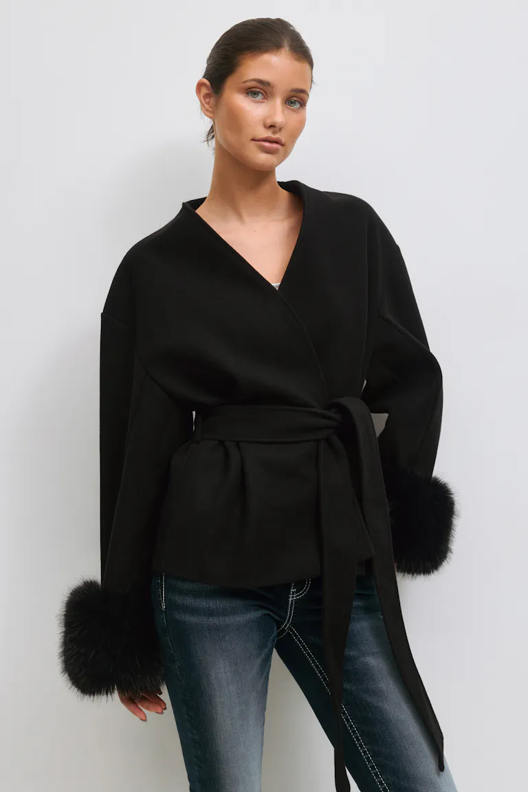 Sort slå-om-jakke med bælte, V-hals og voluminøse ærmer med sorte pelsmanchetter, lagt over en hvid top; sat sammen med falmede slim-fit blå jeans med hvide kontrastsyninger.