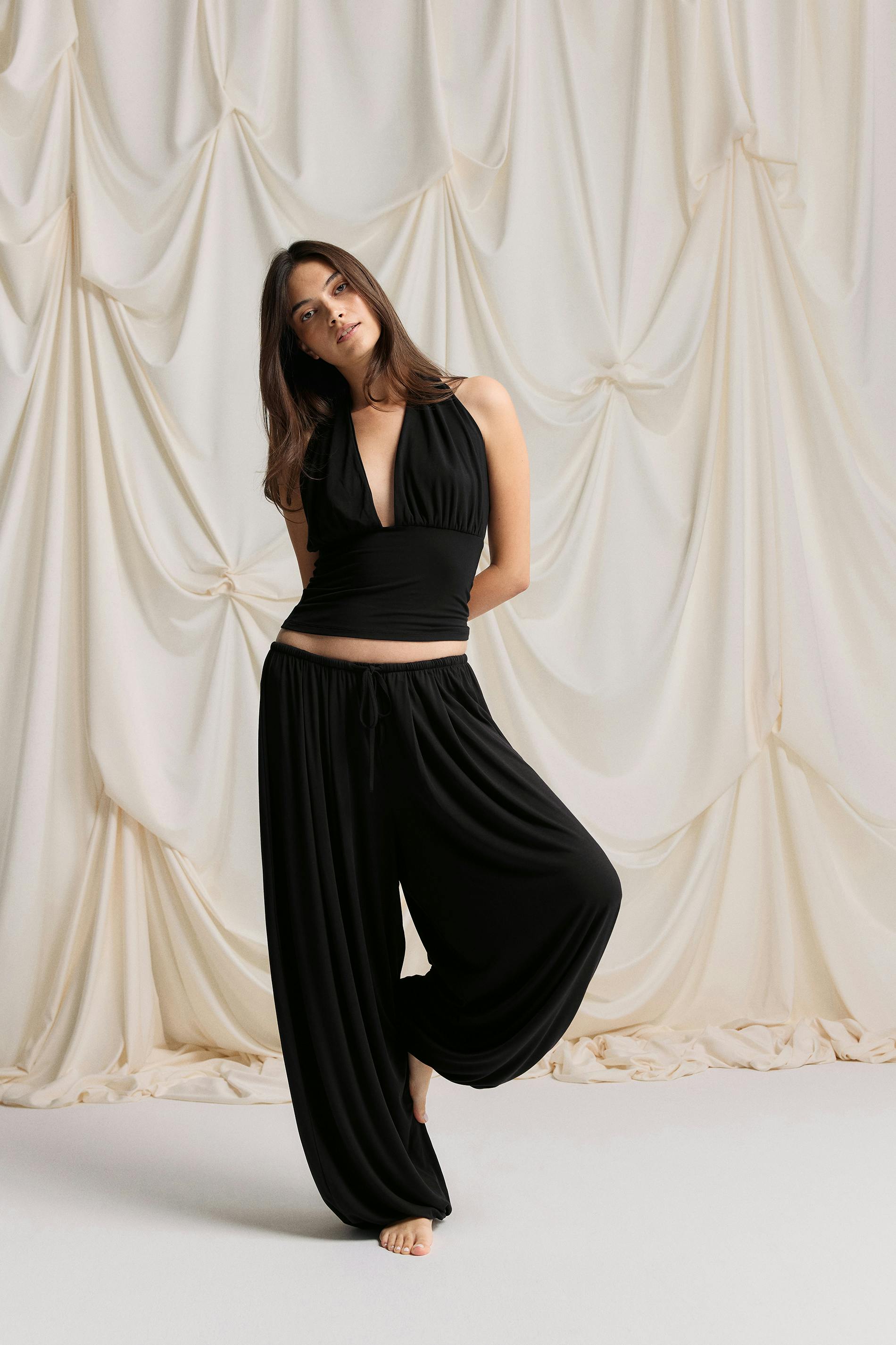 Black halter-neck top with a plunging V-neck and fitted waist, paired with matching black drawstring wide-leg harem trousers.
