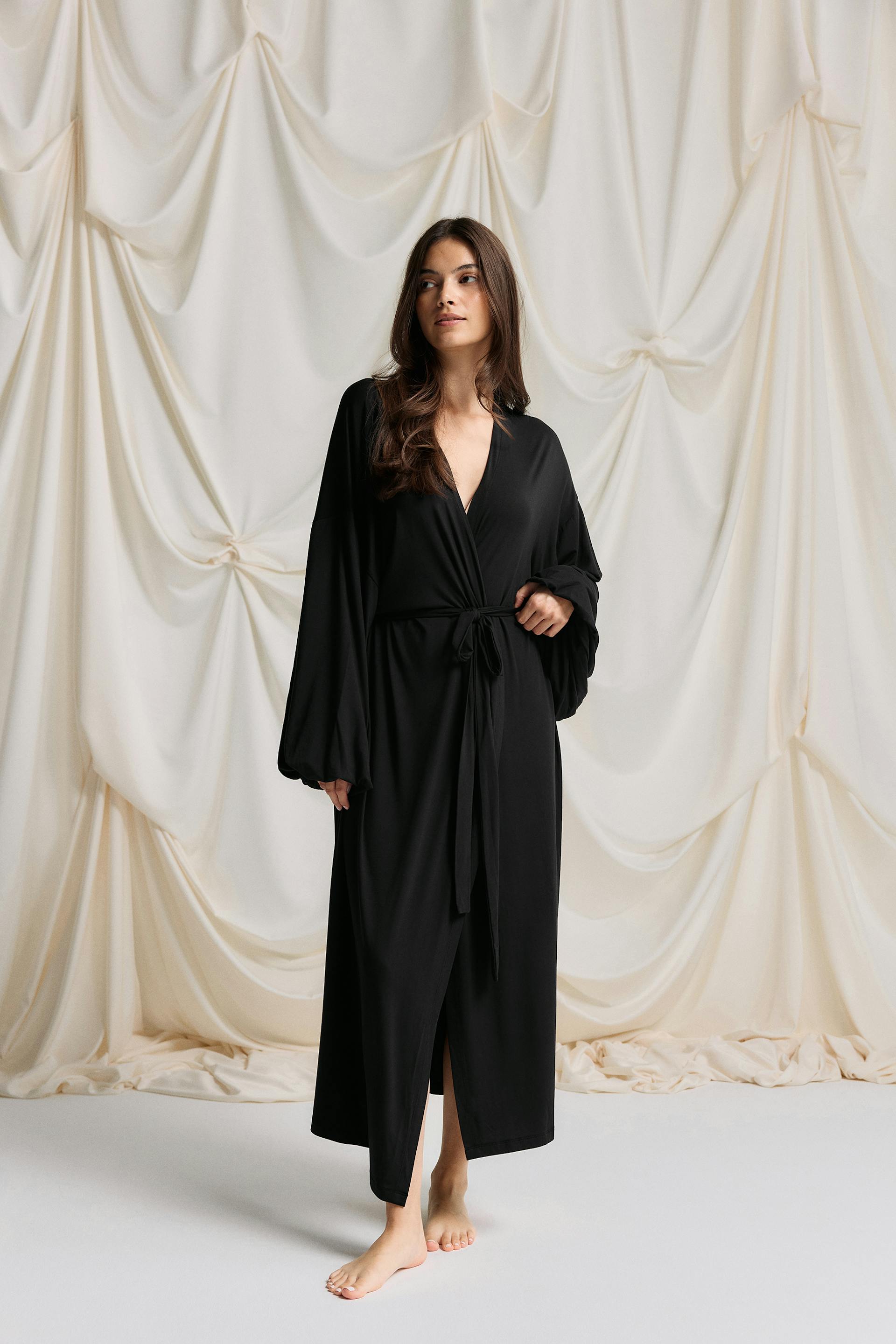 Long black wrap robe with deep V-neck, self-tie waist, voluminous long sleeves and an ankle-length skirt with front slit.