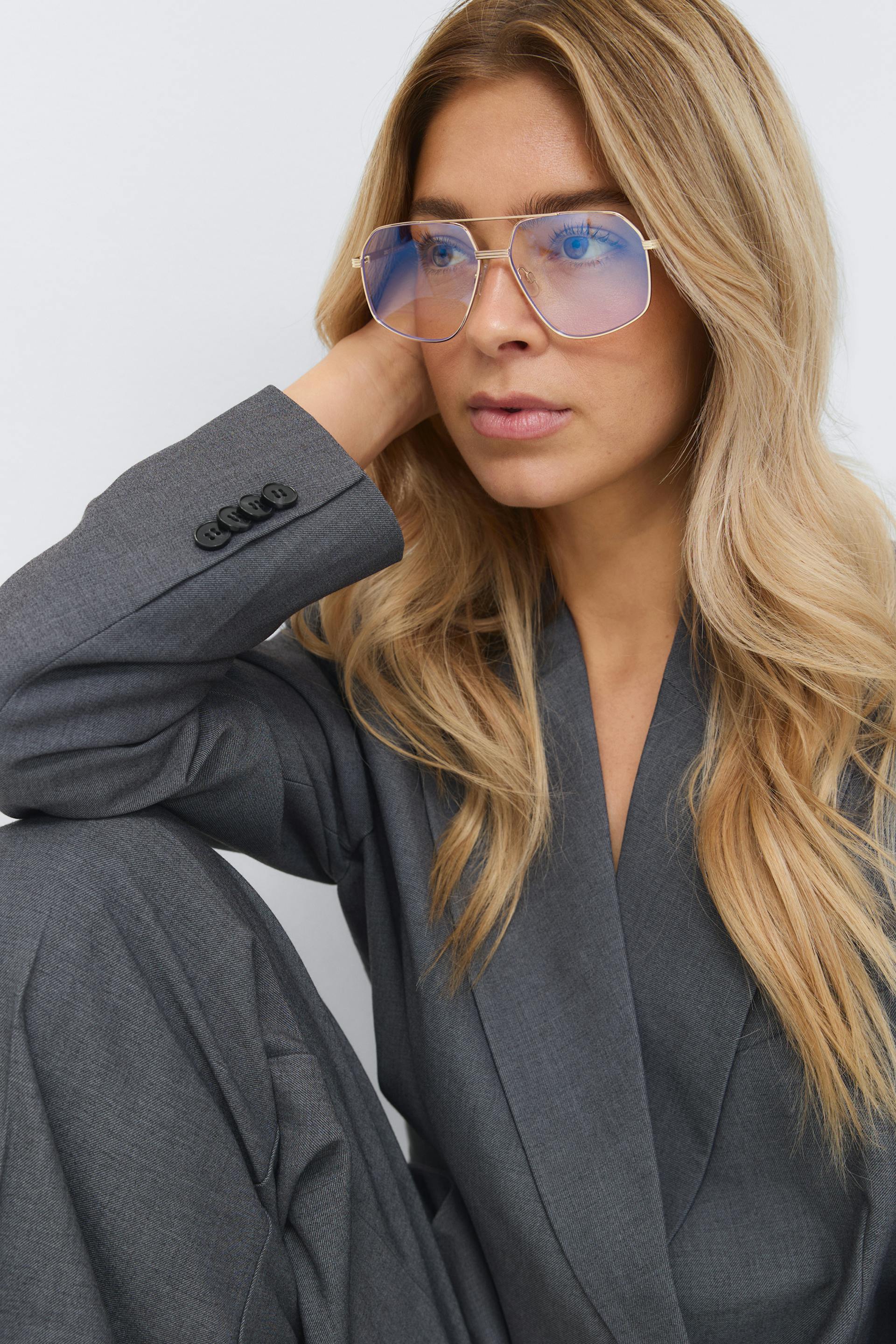 Grå skræddersyet blazer med matchende bukser og ærmeopslag med fire knapper, sammen med guldindfattede pilotsolbriller med blåtonede glas.